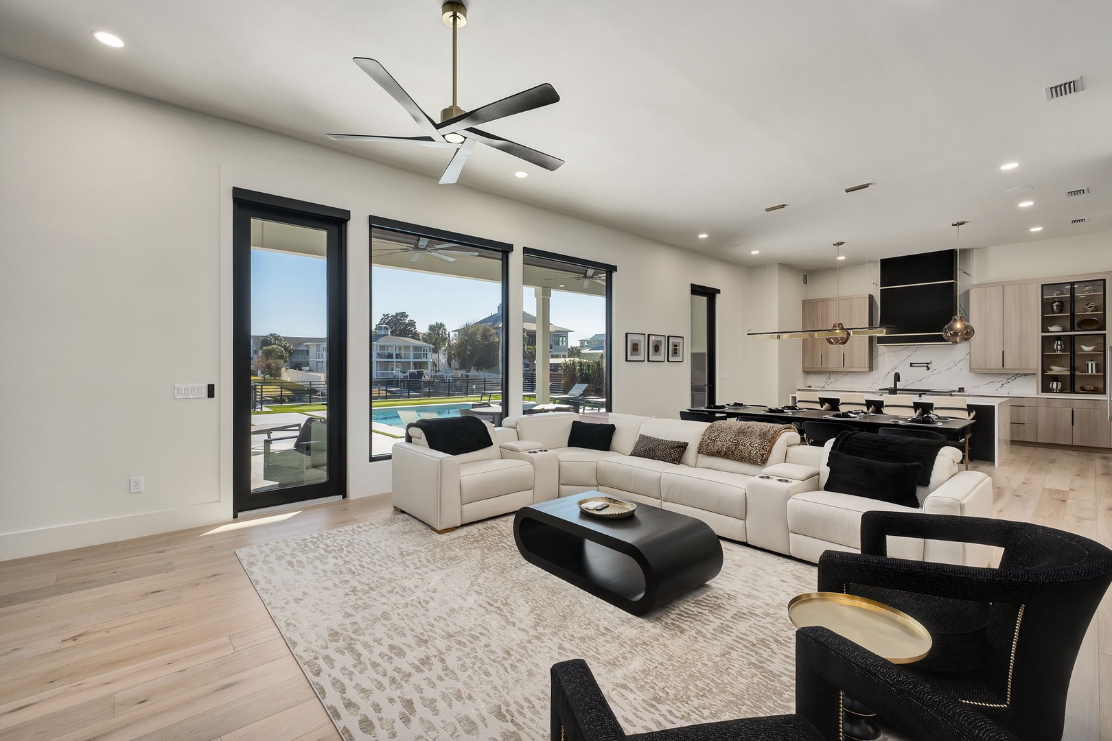 Relax in your spacious open-plan living area with plush sectional seating, modern kitchen, and stunning pool views through floor-to-ceiling windows.