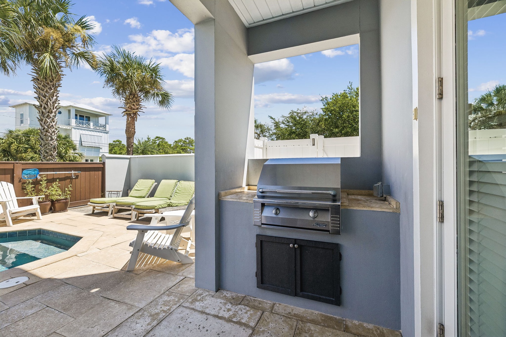 Your own private outdoor oasis awaits—complete with a built-in grill for easy meals, sparkling pool steps away, and lush palm trees framing sunny skies overhead.