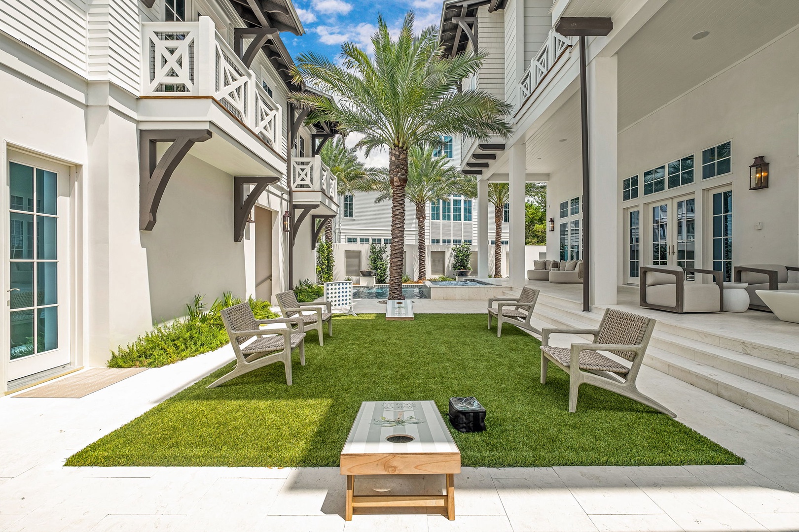 Relax in your private inner courtyard with lush green lawn, swaying palms, and a tranquil fountain—a serene oasis framed by elegant architecture and inviting lounge seating.