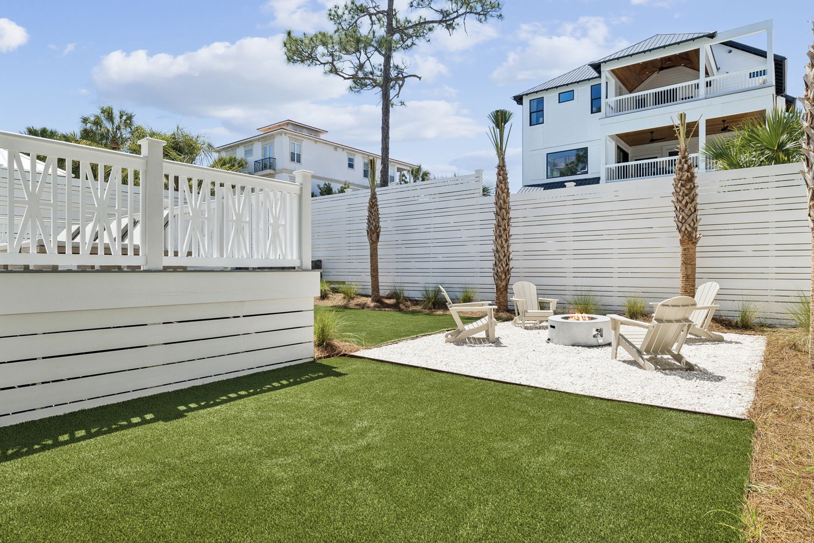 Relax in your private backyard oasis with soft turf, cozy fire pit seating, and tropical palms creating the perfect outdoor retreat.