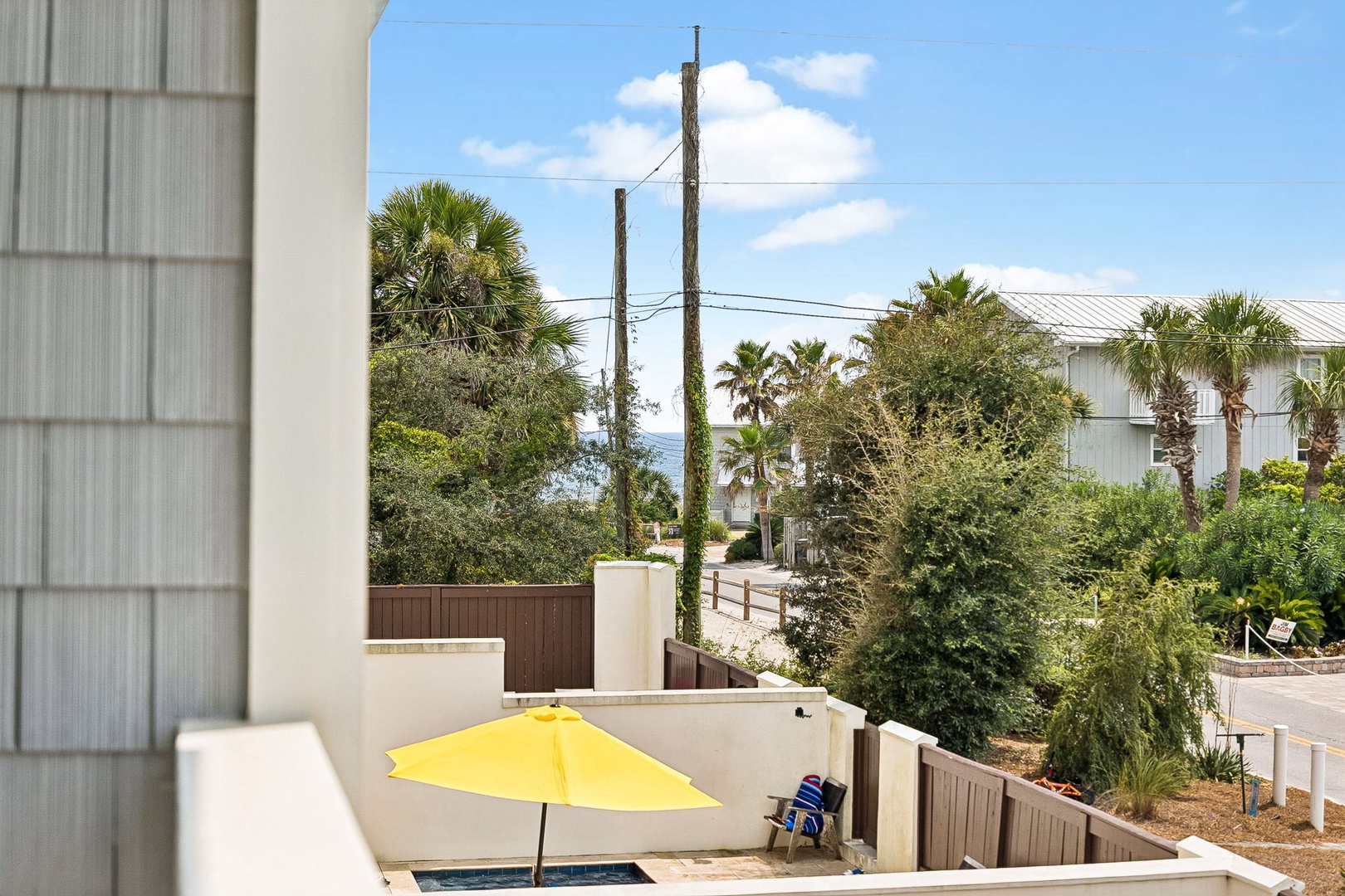 Glimpse ocean views and swaying palms from your private patio, where a cheerful yellow umbrella and hot tub invite you to unwind in this coastal setting.