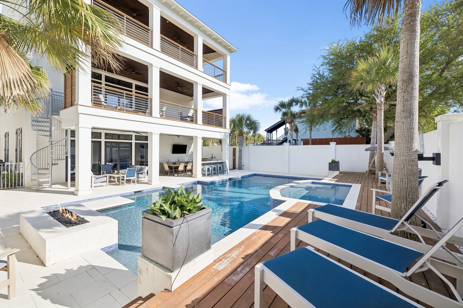 Modern three-story luxury vacation home featuring a pristine swimming pool, tropical palm trees, and contemporary architecture in a private setting.