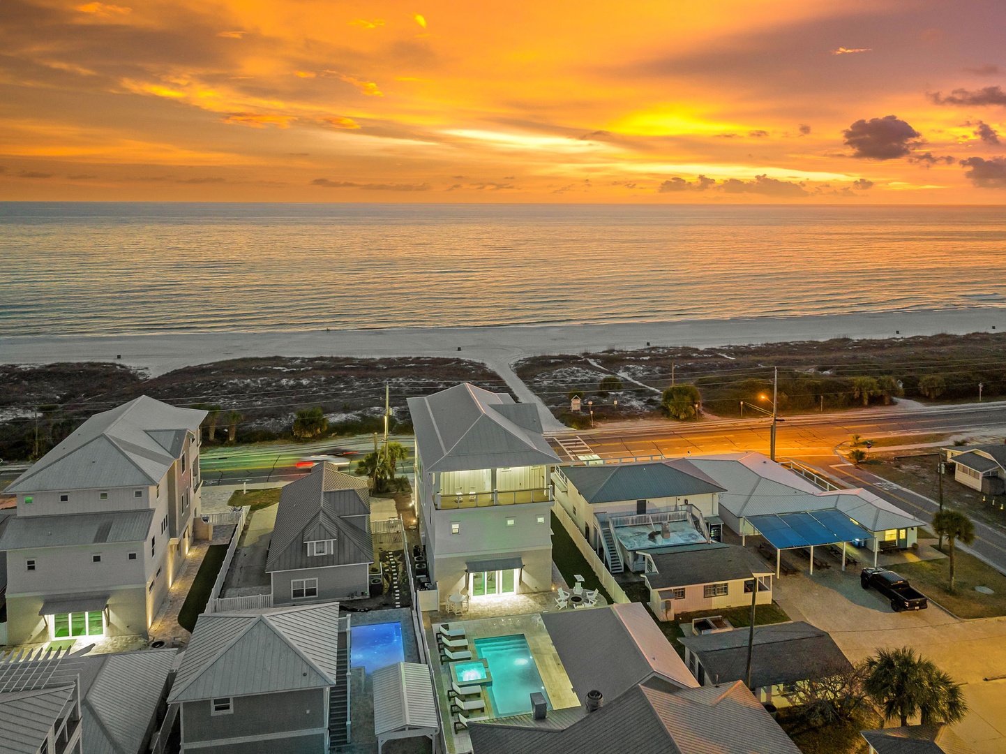 Dramatic sunset paints the sky in golden hues over beachfront properties and the shimmering ocean.
