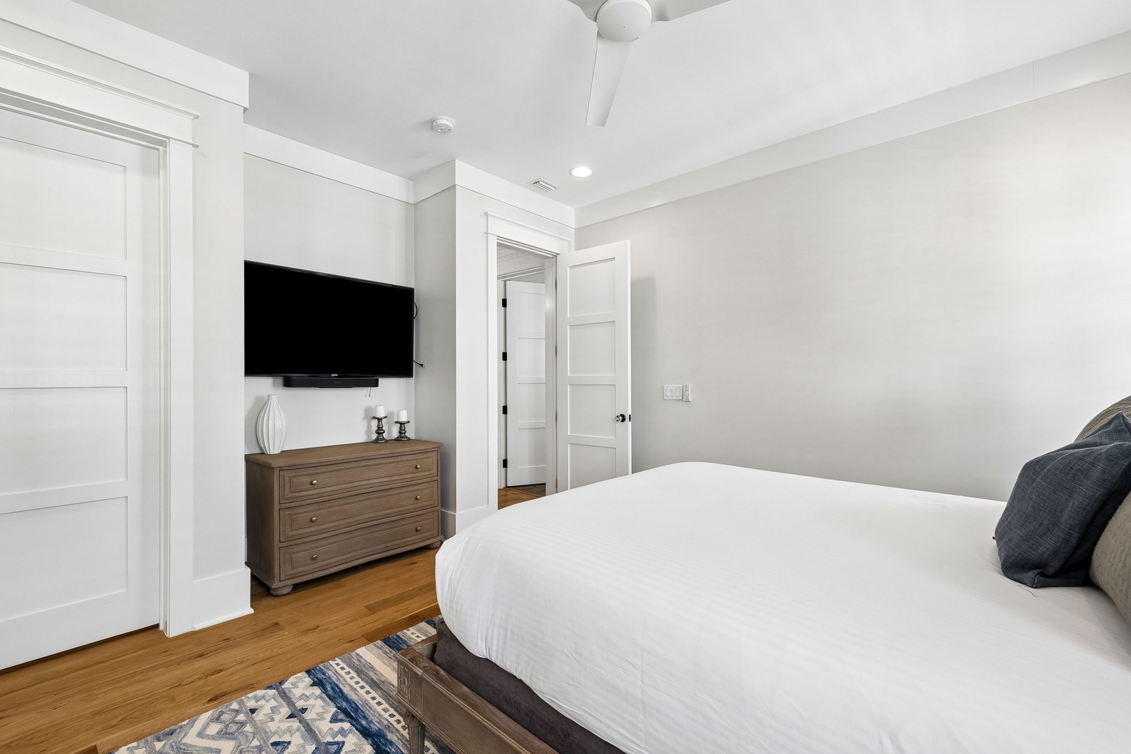 Sink into crisp white linens in your serene bedroom, where warm wood floors and coastal touches create a peaceful retreat for restful nights.