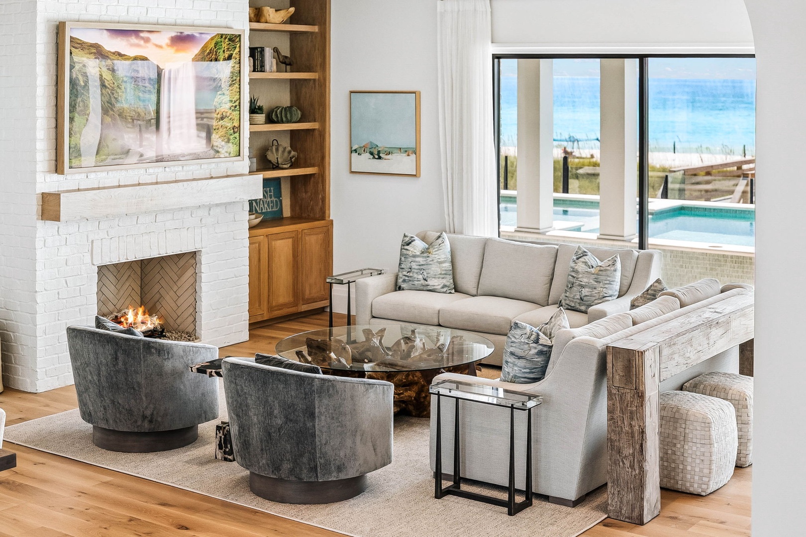 Sink into plush seating while waves roll in beyond your window and a warm fire glows nearby. This inviting living space blends coastal charm with modern comfort—perfect for unwinding after a day at the beach.