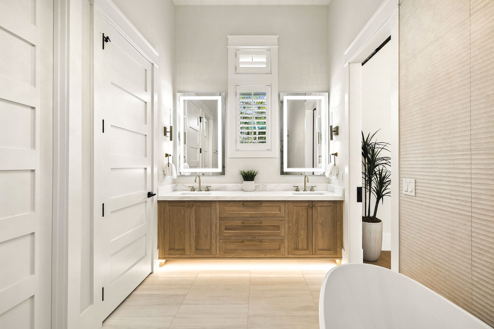 Step into your serene spa-inspired bathroom, where natural light floods through plantation shutters, illuminating dual vanities with elegant mirrors and warm wood cabinetry that creates a calming, luxurious retreat.