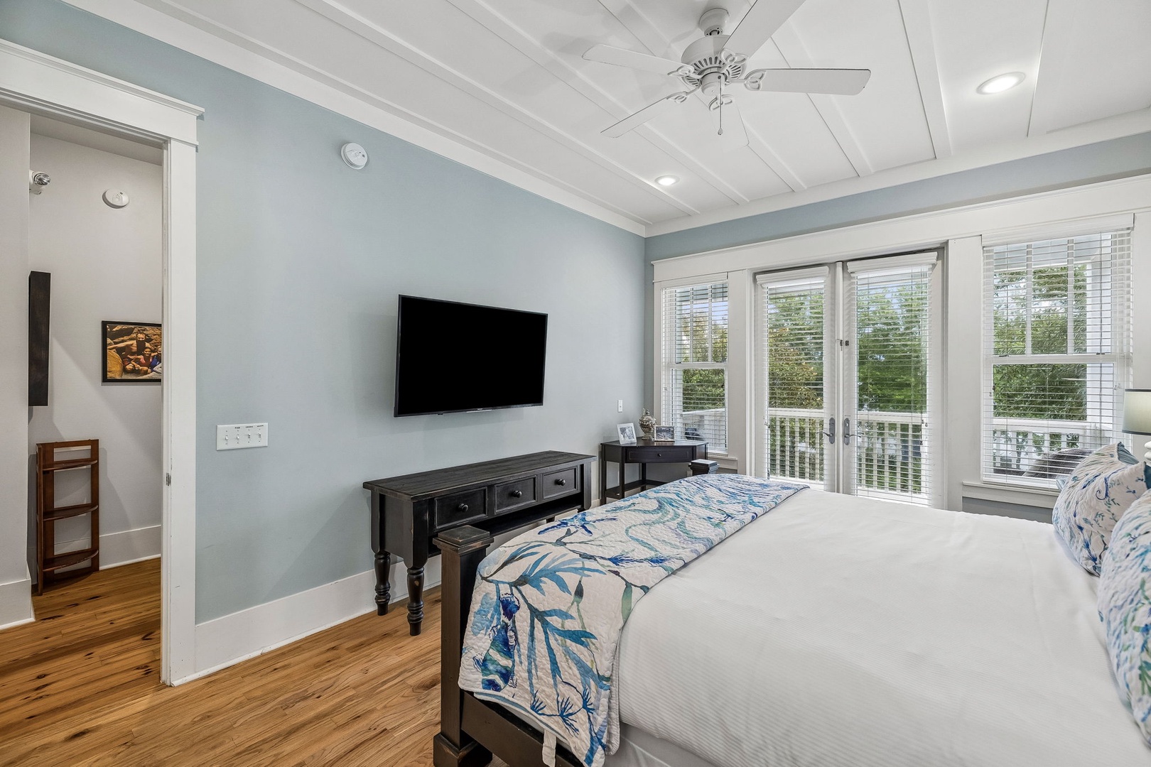 Relax in your bright, coastal-inspired bedroom with French doors opening to a private balcony overlooking lush greenery. Crisp linens and calming blue tones create a serene retreat.