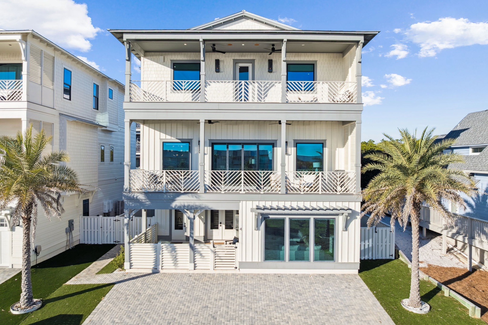Beautiful three-story coastal home with elegant white siding, decorative railings, and palm trees framing the entrance.