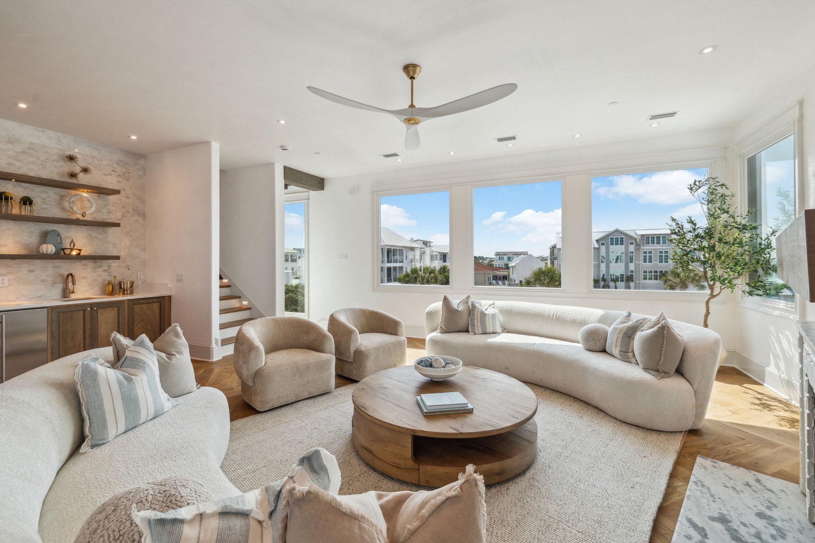 Sink into plush coastal elegance in your sun-drenched living space, where oversized windows frame neighborhood views and a gentle ceiling fan keeps you cool as you unwind.