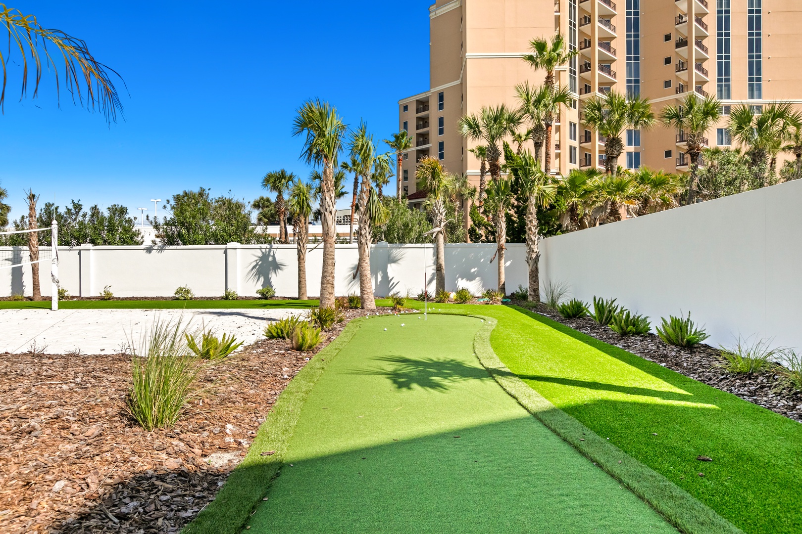 A putting green winds through landscaped gardens with swaying palms and a clear blue sky. Ideal for practicing your swing or enjoying leisurely afternoons outdoors.