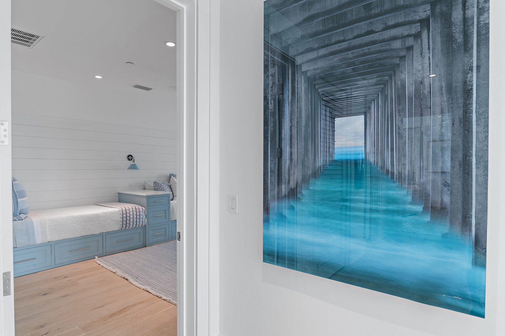 Step into your serene coastal retreat through a hallway lined with soothing ocean-inspired artwork. The built-in bed with ample storage welcomes you to unpack and unwind in this peaceful guest room.