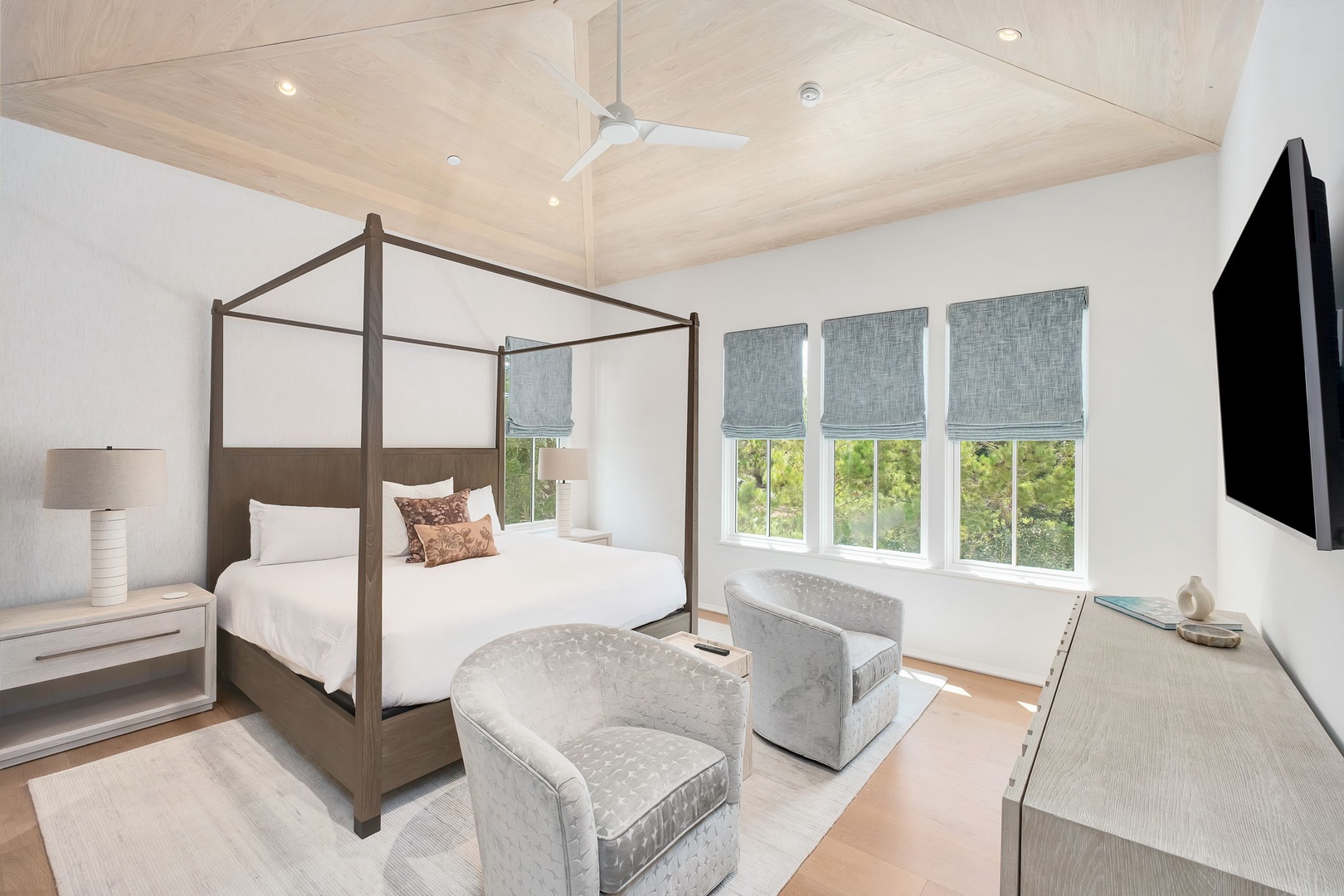 Unwind in your serene bedroom with crisp linens, plush seating, and natural light streaming through windows overlooking lush greenery—your perfect coastal retreat.