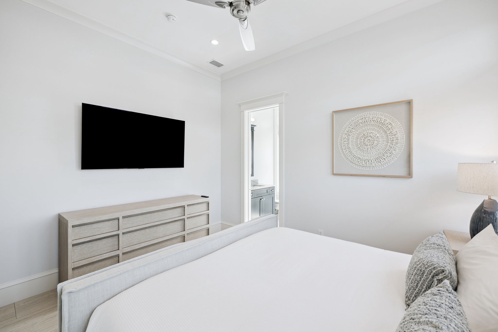 Unwind in your serene bedroom featuring crisp white linens, modern furnishings, and a wall-mounted TV for cozy nights in.