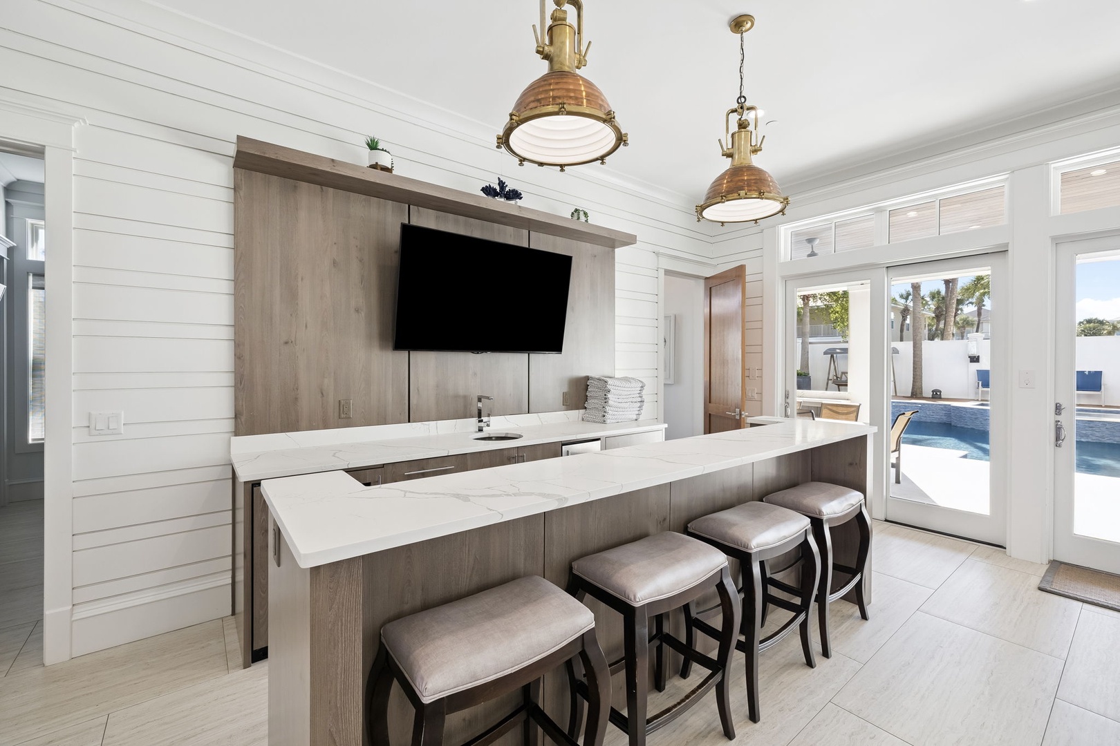 Gather around this sleek kitchen island where coastal charm meets modern luxury, perfect for morning coffee or evening cocktails while watching the pool.