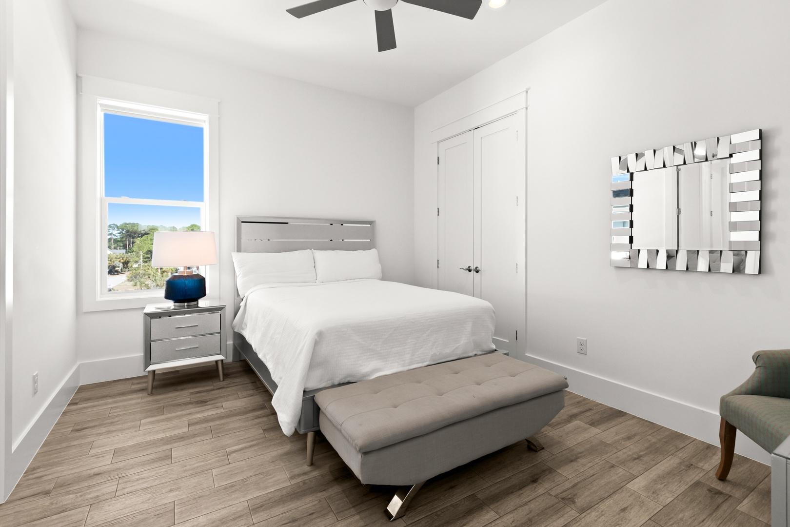 Relax in this bright, modern bedroom with crisp linens, a cozy bench, and a stylish ceiling fan overhead. Natural light pours in, creating a peaceful retreat for your stay.