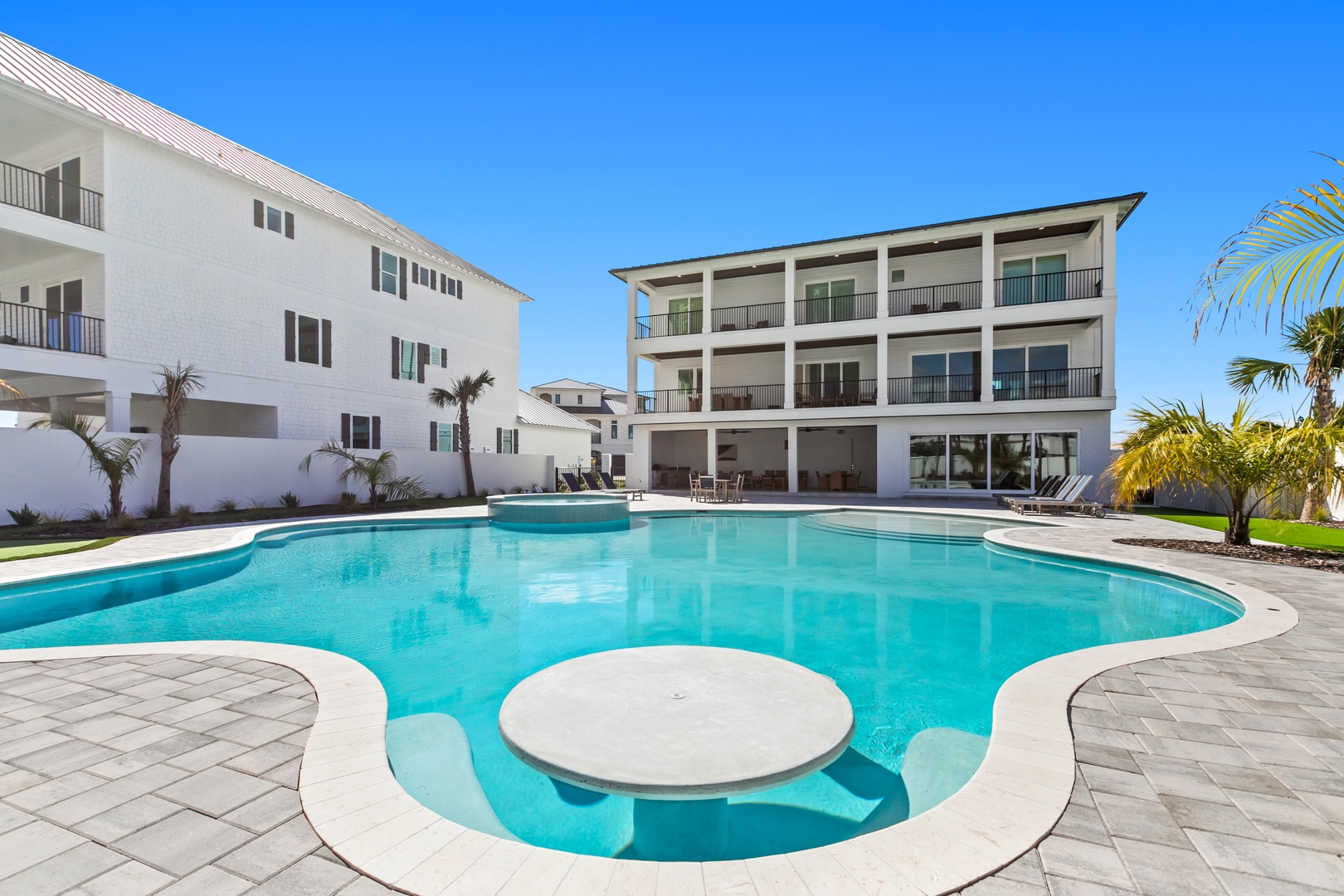 Stunning resort-style pool with unique design features and modern buildings set against clear blue skies and tropical landscaping in the surrounding area.