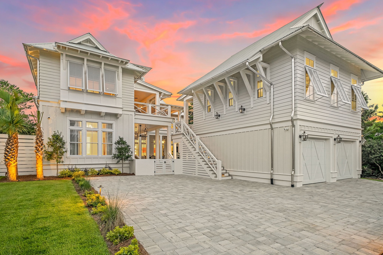 A stunning coastal-style retreat captures the golden hour glow, where elegant architecture meets inviting southern charm. The spacious driveway and beautifully landscaped grounds set the scene for an unforgettable arrival.