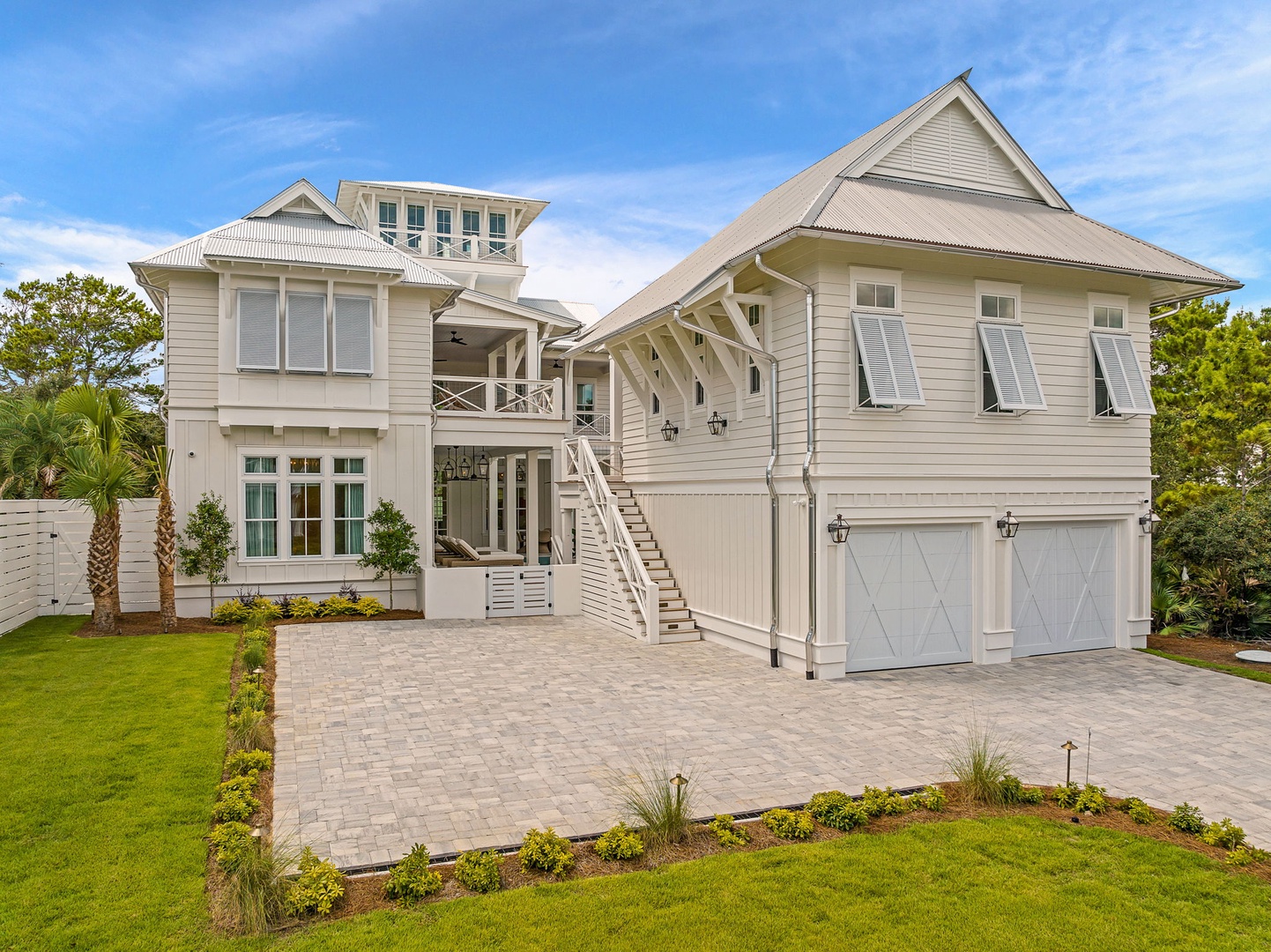This coastal retreat features classic architecture with its distinctive peaked rooflines, welcoming covered entryway, and spacious driveway framed by lush tropical landscaping and mature palms.