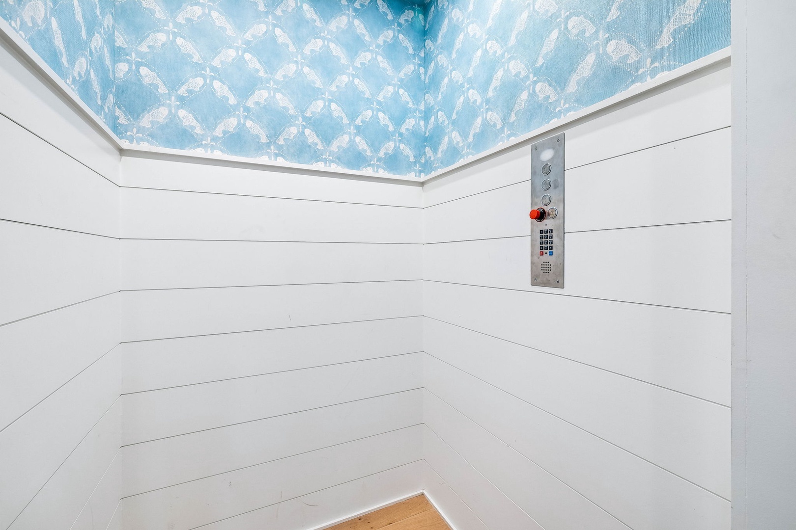 The elevator features charming white shiplap walls and a whimsical blue sky ceiling mural with clouds, adding a unique artistic touch to your vertical journey.