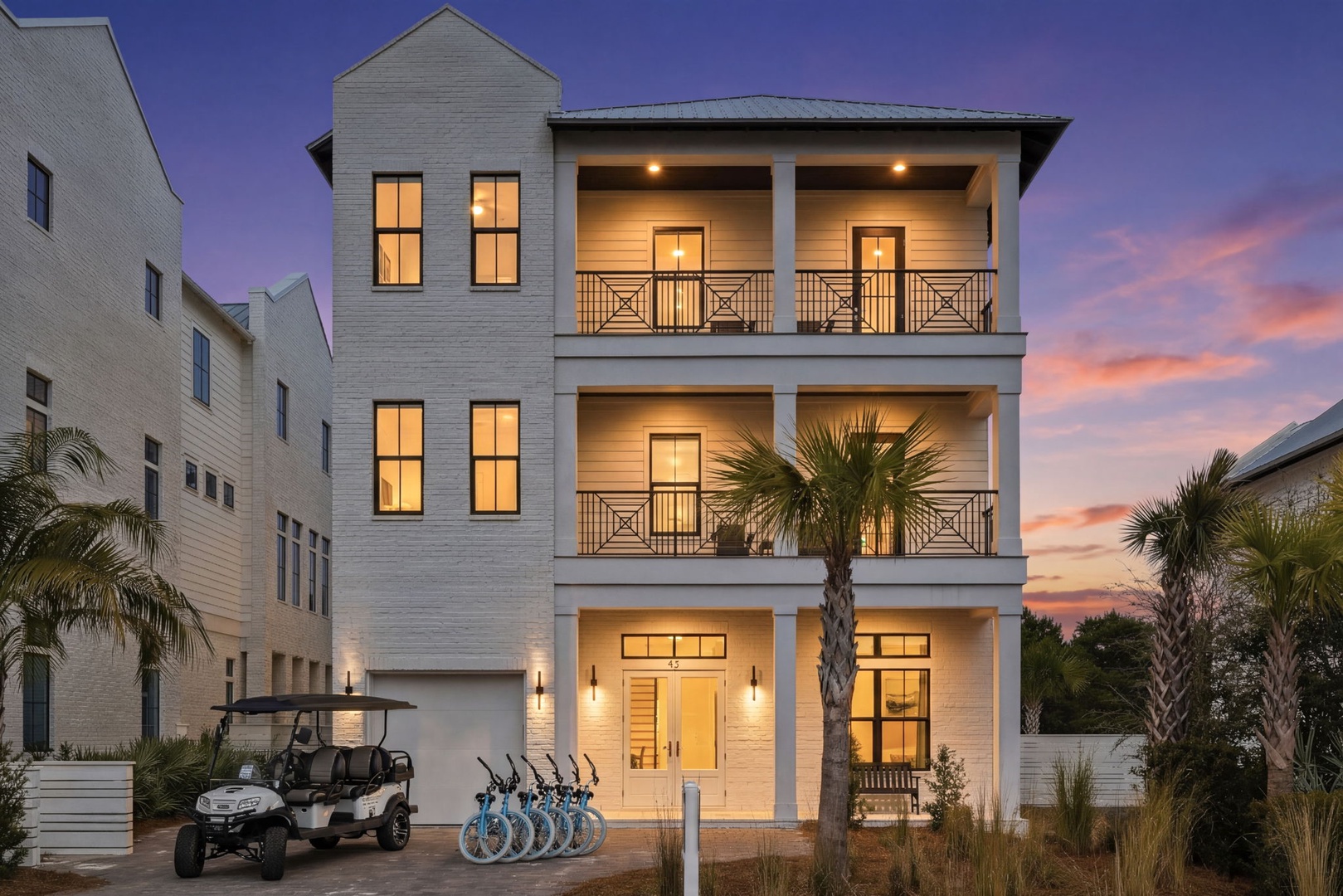 Elegant three-story coastal home featuring multiple covered balconies and tropical landscaping captured during a stunning twilight hour.