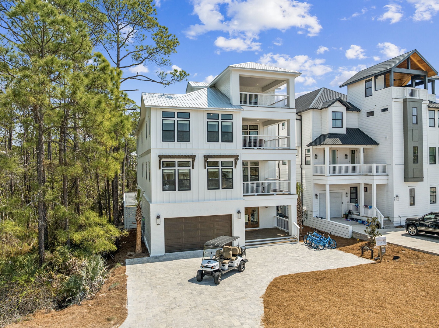 Modern coastal home nestled among lush pine trees, featuring multiple balconies and contemporary architecture in a peaceful residential setting.