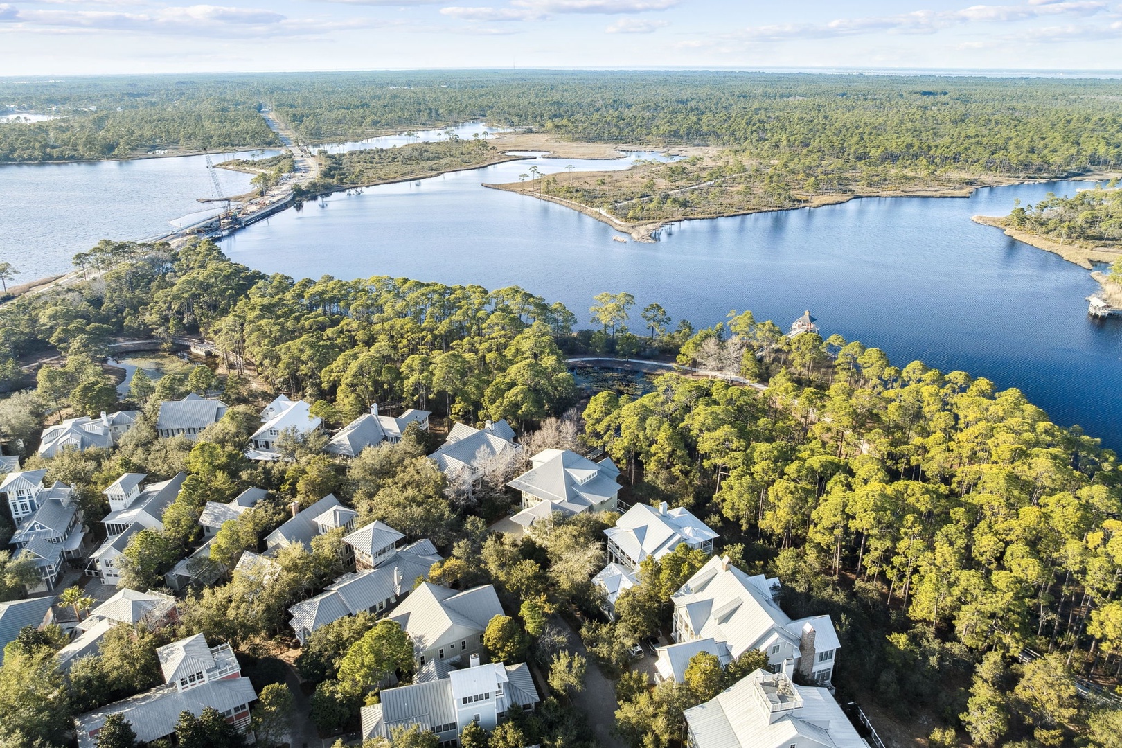 Aerial view showcases a peaceful lakefront community with white-roofed homes nestled among lush trees beside pristine waters.