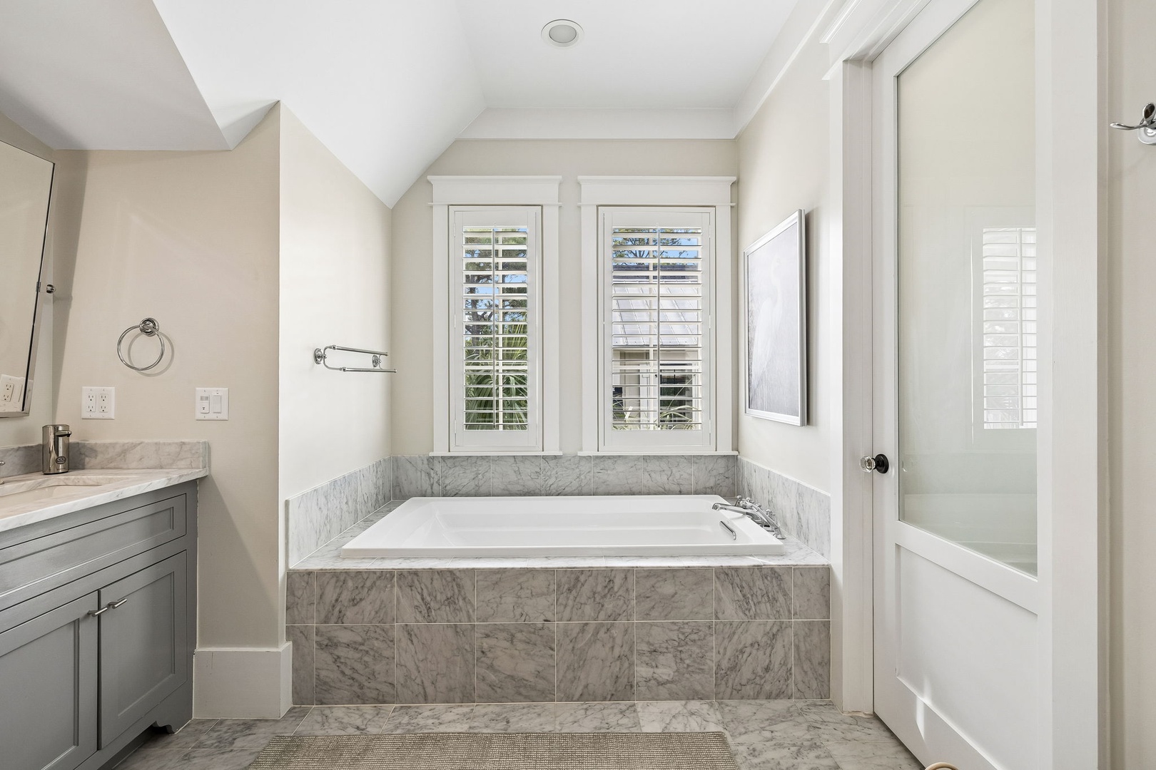 Soak away the day in your elegant marble-lined tub, framed by soft natural light filtering through plantation shutters and a vaulted ceiling that adds an airy, spa-like feel.