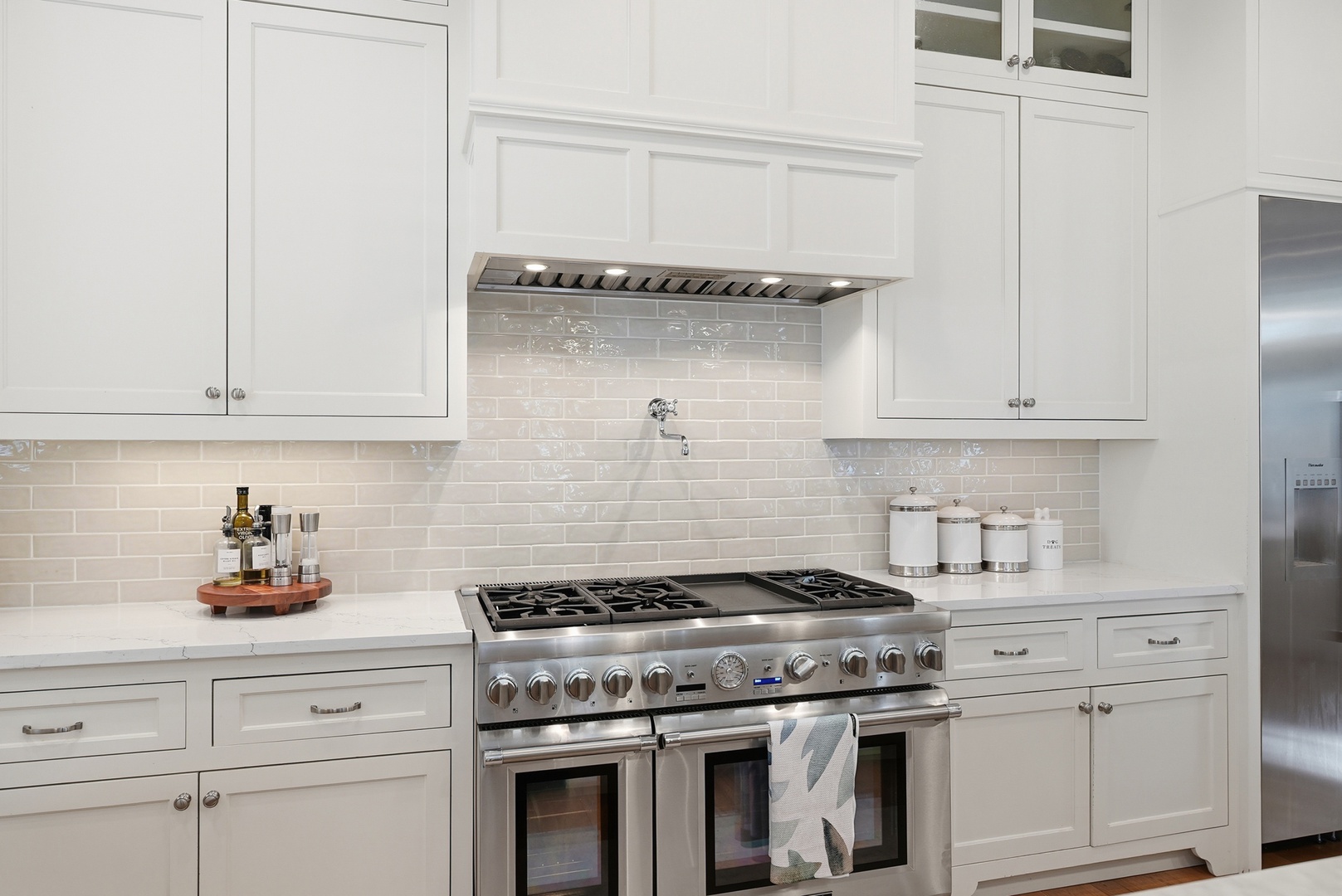 A bright, fully-equipped kitchen with white cabinetry, sleek subway tile, and a professional-grade gas range to bring your favorite recipes to life.