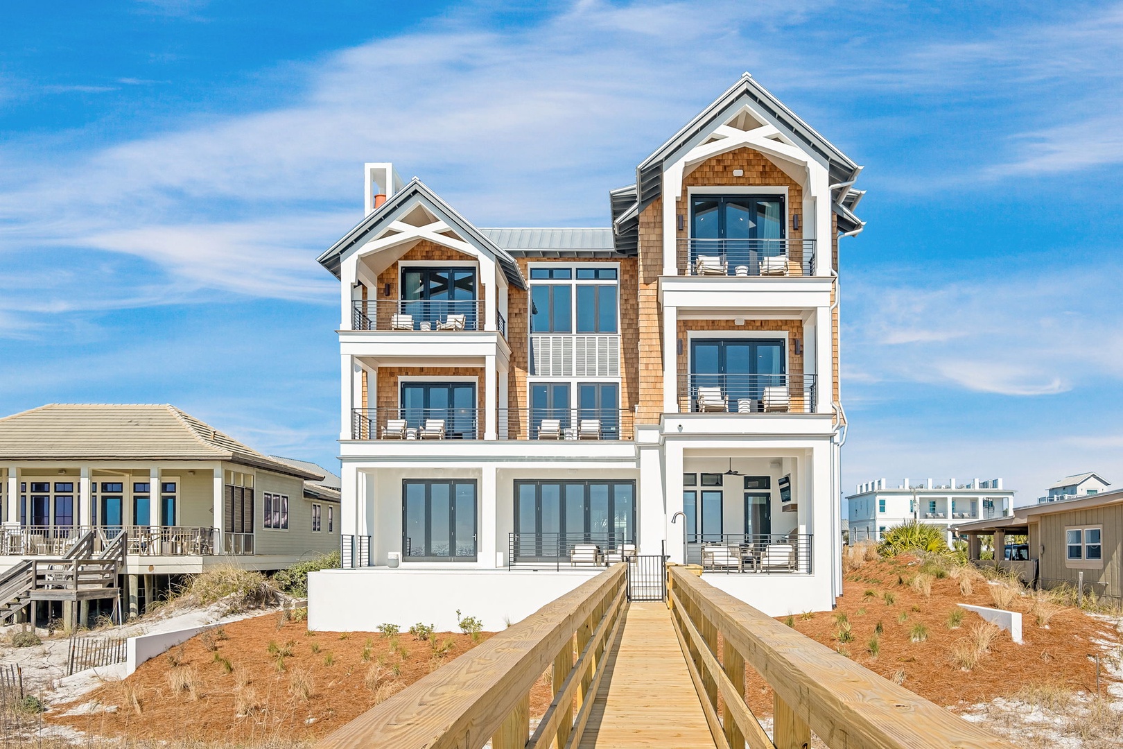 This impressive beachfront property features multiple levels with private balconies and panoramic views. The wooden walkway leads directly to this stunning coastal retreat.