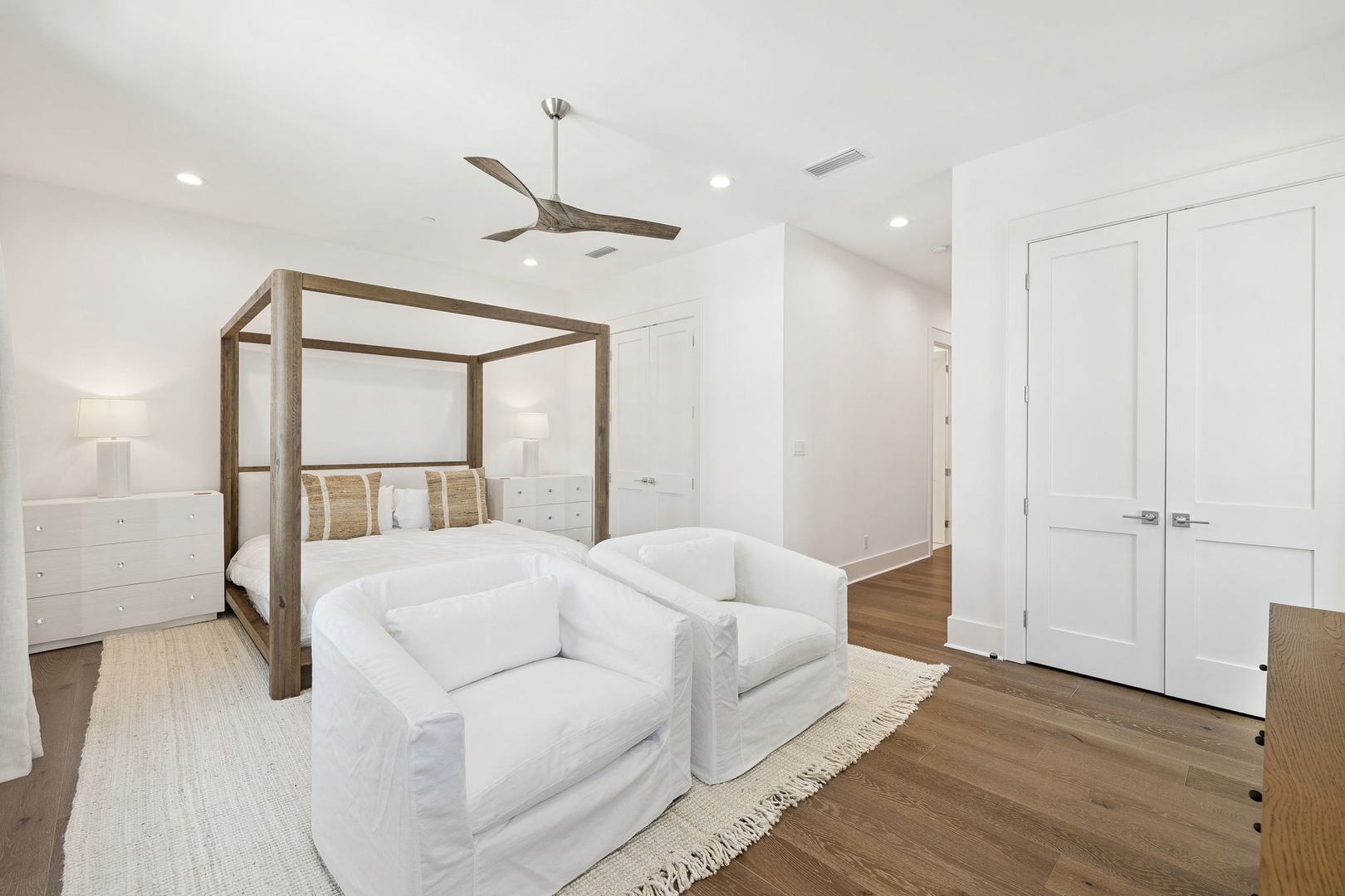 Sink into plush seating beside your elegant four-poster bed, where modern luxury meets comfort in this serene white retreat.