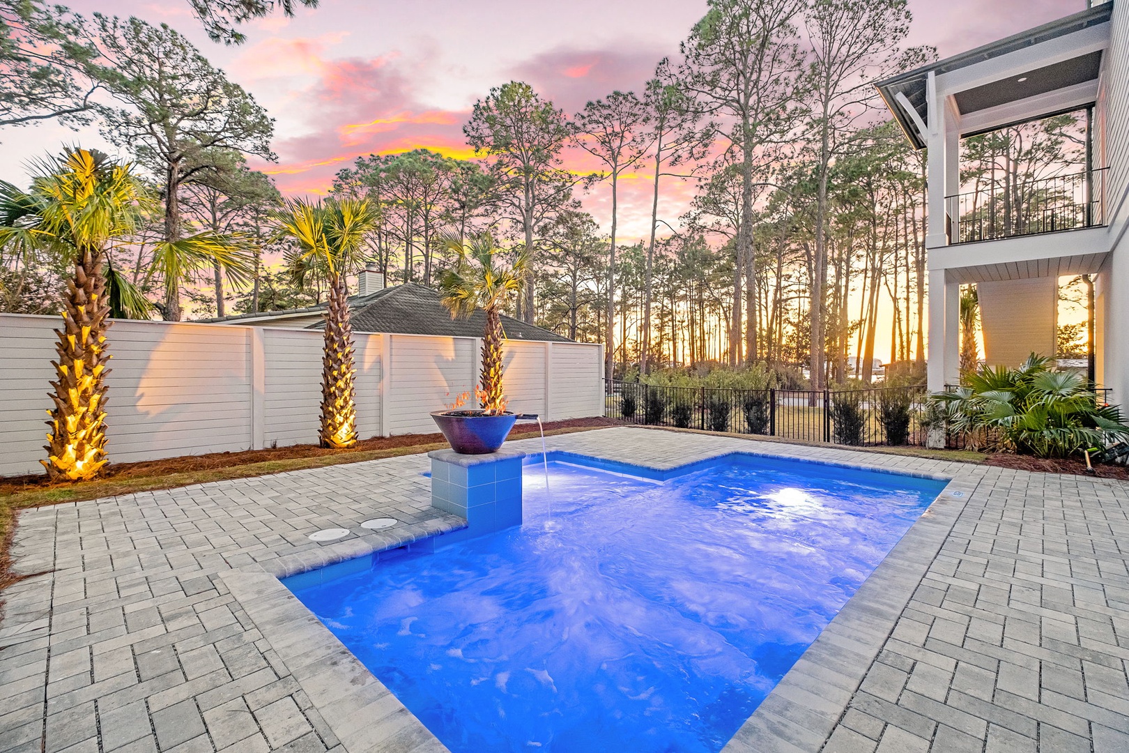 Stunning sunset paints the sky in vibrant hues over the private pool area, surrounded by lush landscaping and mature trees.