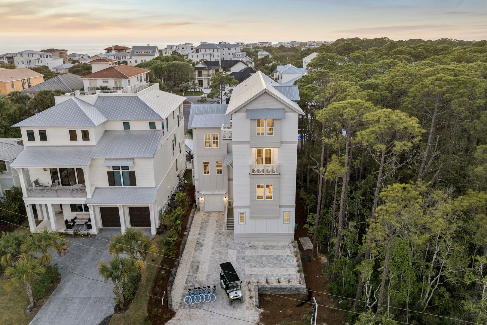 Aerial view of coastal vacation properties nestled among lush forest canopy in a charming beach community.