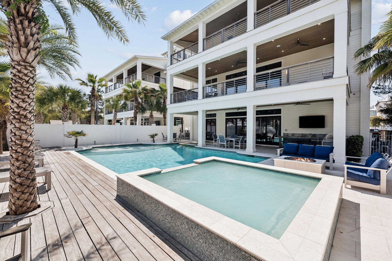 Modern beachside villa featuring a sparkling pool and hot tub surrounded by swaying palms and contemporary architecture.