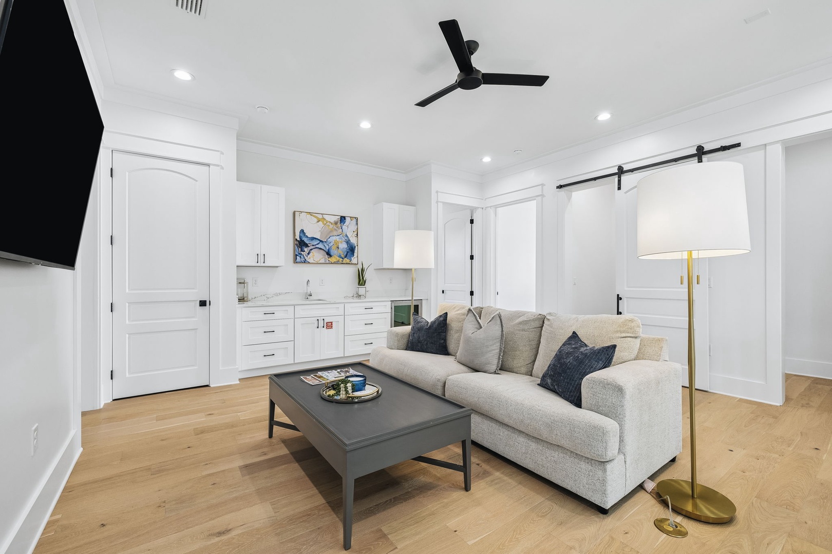 Unwind in your stylish living area, where a plush sofa invites you to relax beneath warm lighting and a cool ceiling fan, with a sleek kitchenette at your fingertips.