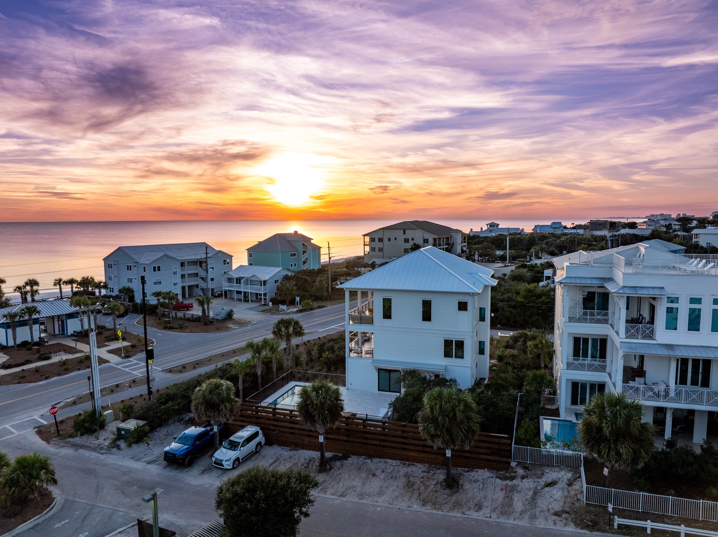 Stunning aerial view of the beachfront property at sunset, showcasing the coastal neighborhood and nearby vacation rental homes.