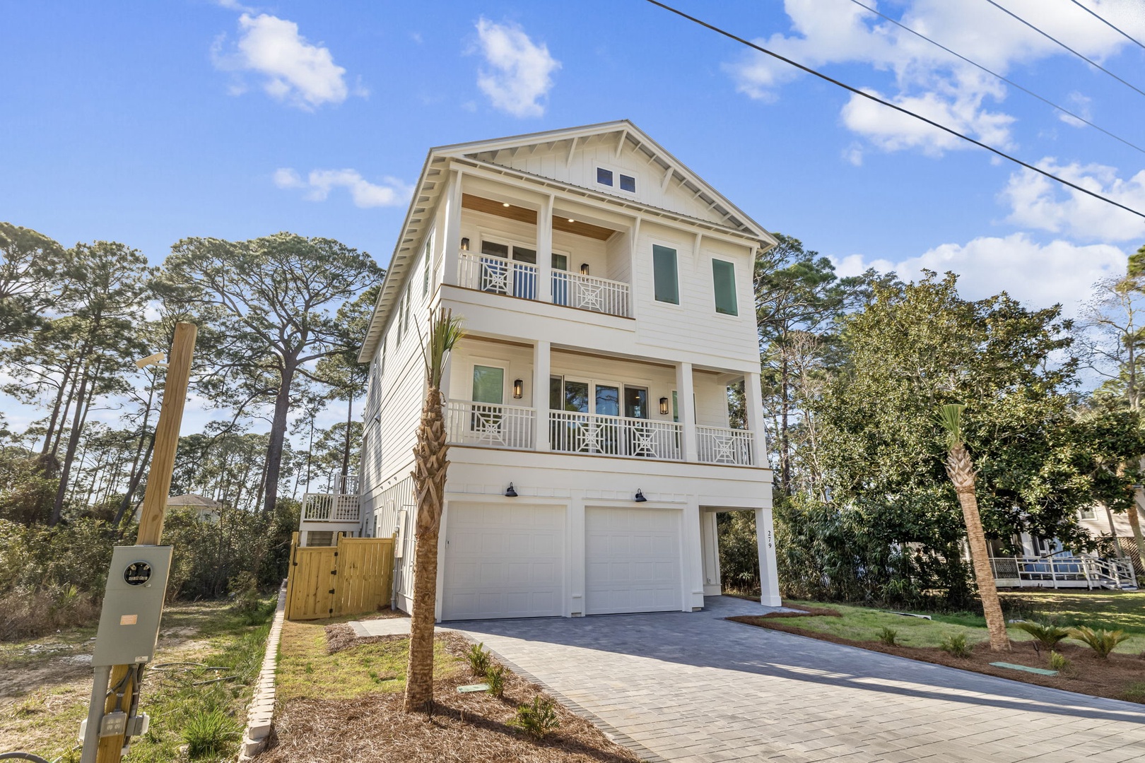 A stunning three-story coastal home with spacious balconies and garage parking, nestled among towering trees in a peaceful neighborhood setting.