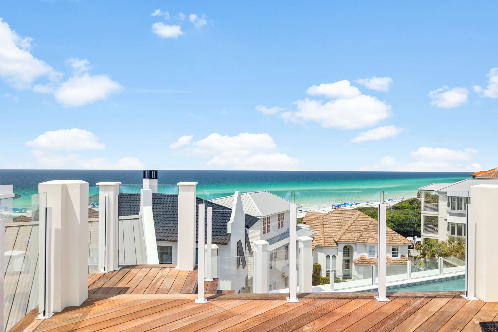 Elevated terrace overlooking turquoise waters and white-sand beaches, with partial pool views and coastal architecture below. Part of the surrounding beachfront neighborhood.