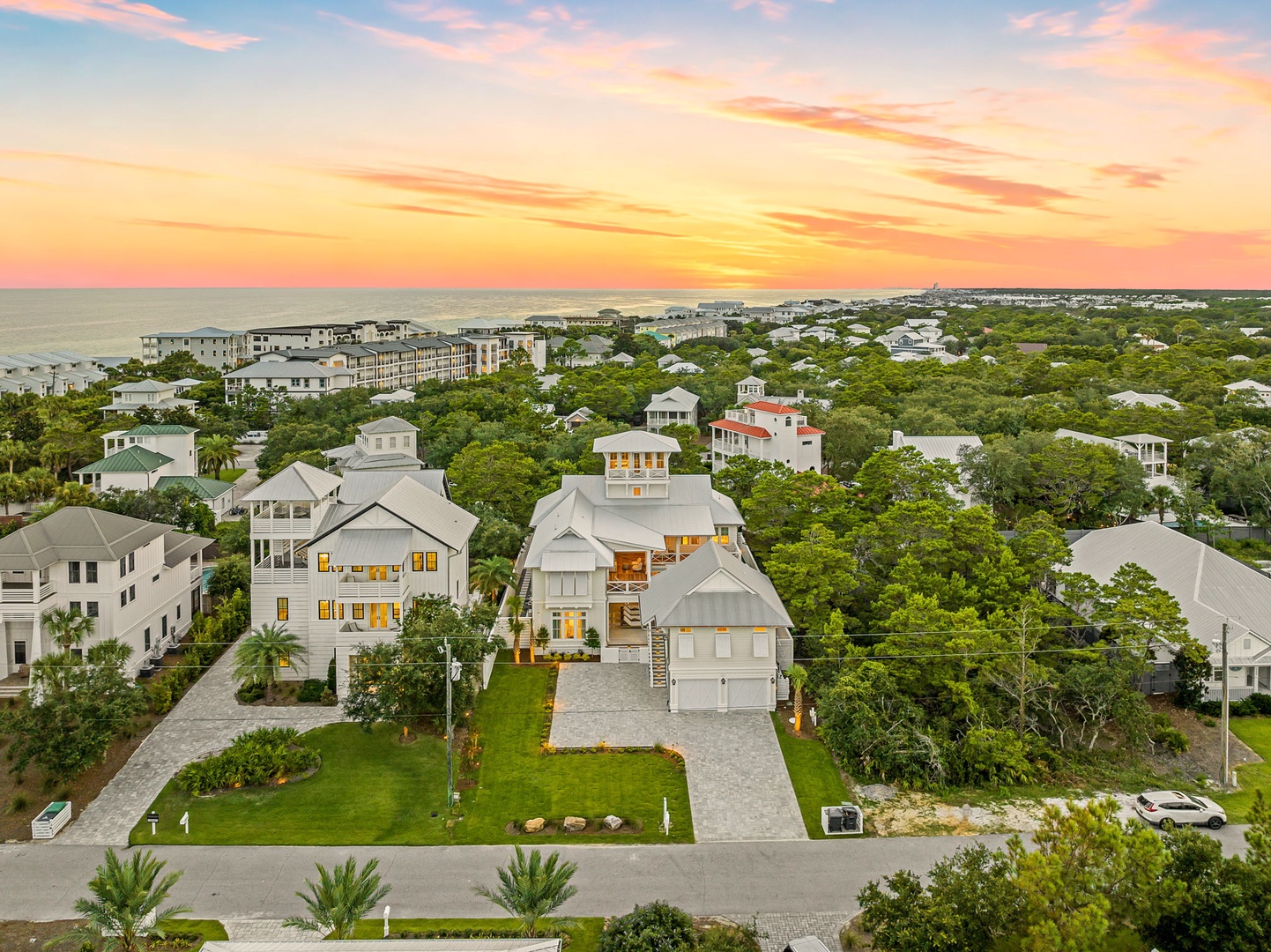 Stunning aerial view of a coastal neighborhood captures the property nestled among lush greenery, with the beach and ocean just beyond. The golden sunset paints the sky, showcasing the serene coastal setting.