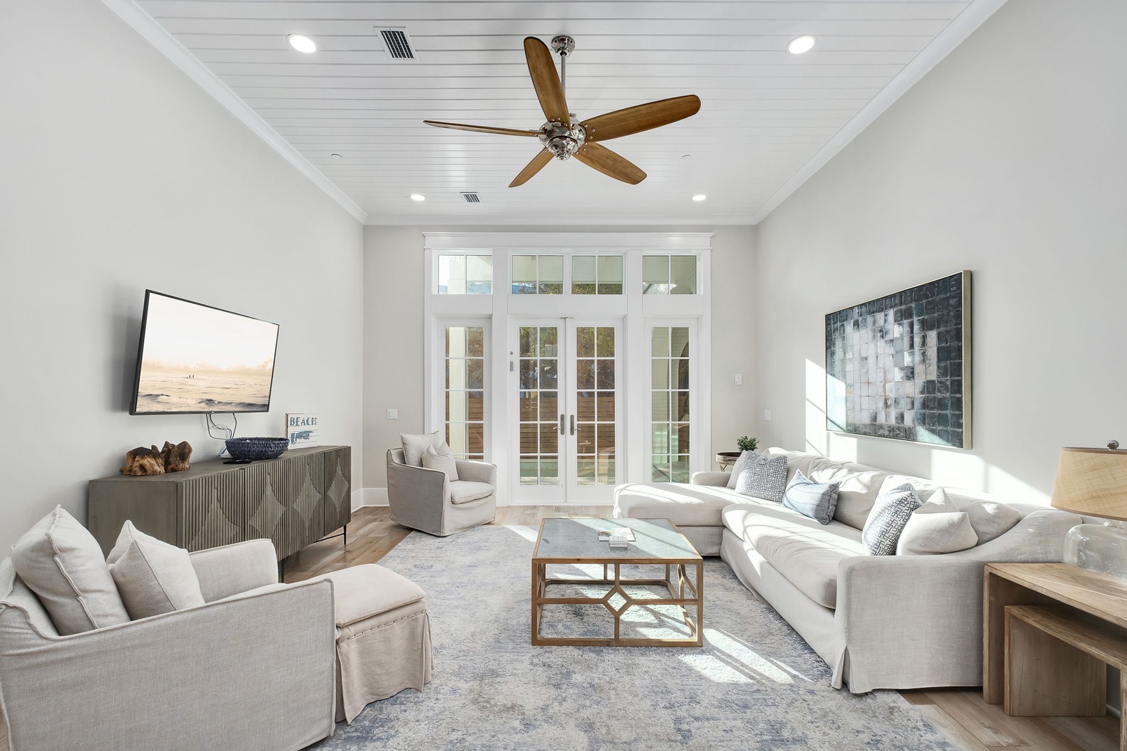 Relax in your bright living room with plush seating, smart TV, and peaceful garden views through elegant French doors.