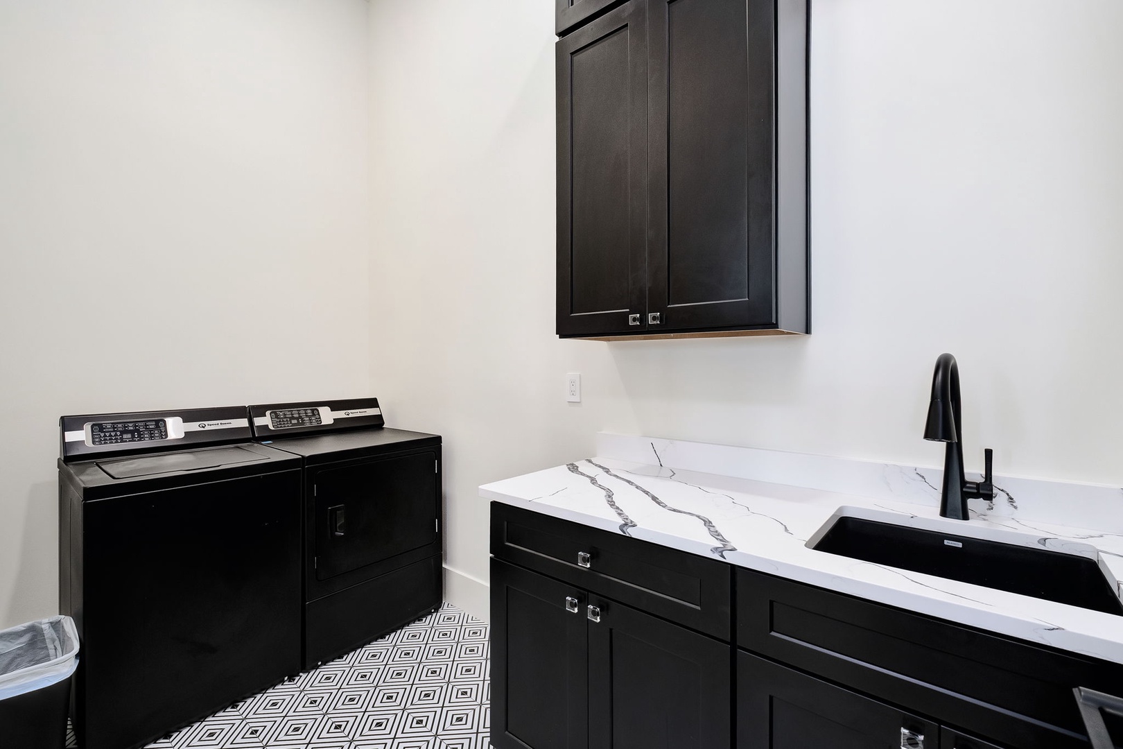 Your stylish laundry room features elegant black cabinetry, marble countertops, and modern appliances for convenient in-home washing.