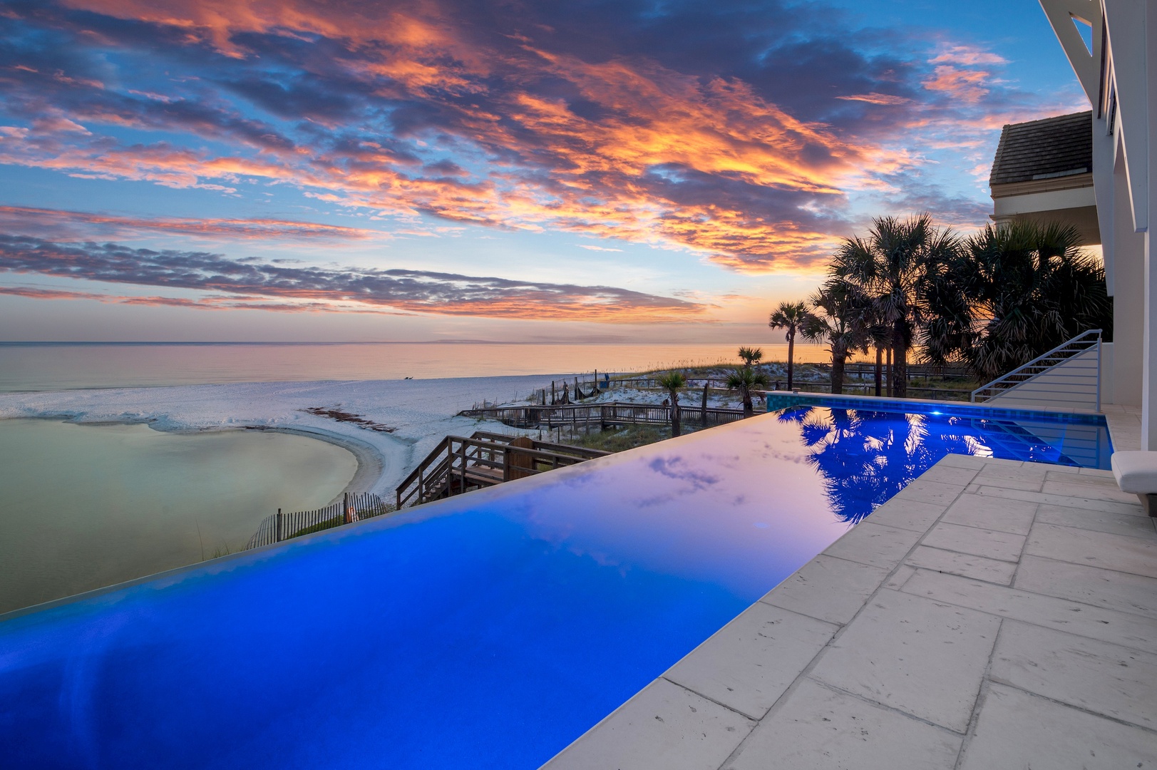 A stunning sunset paints the sky in fiery orange and pink hues above the private infinity pool and beachfront. Palm trees sway gently as the day ends, creating an unforgettable coastal paradise backdrop.