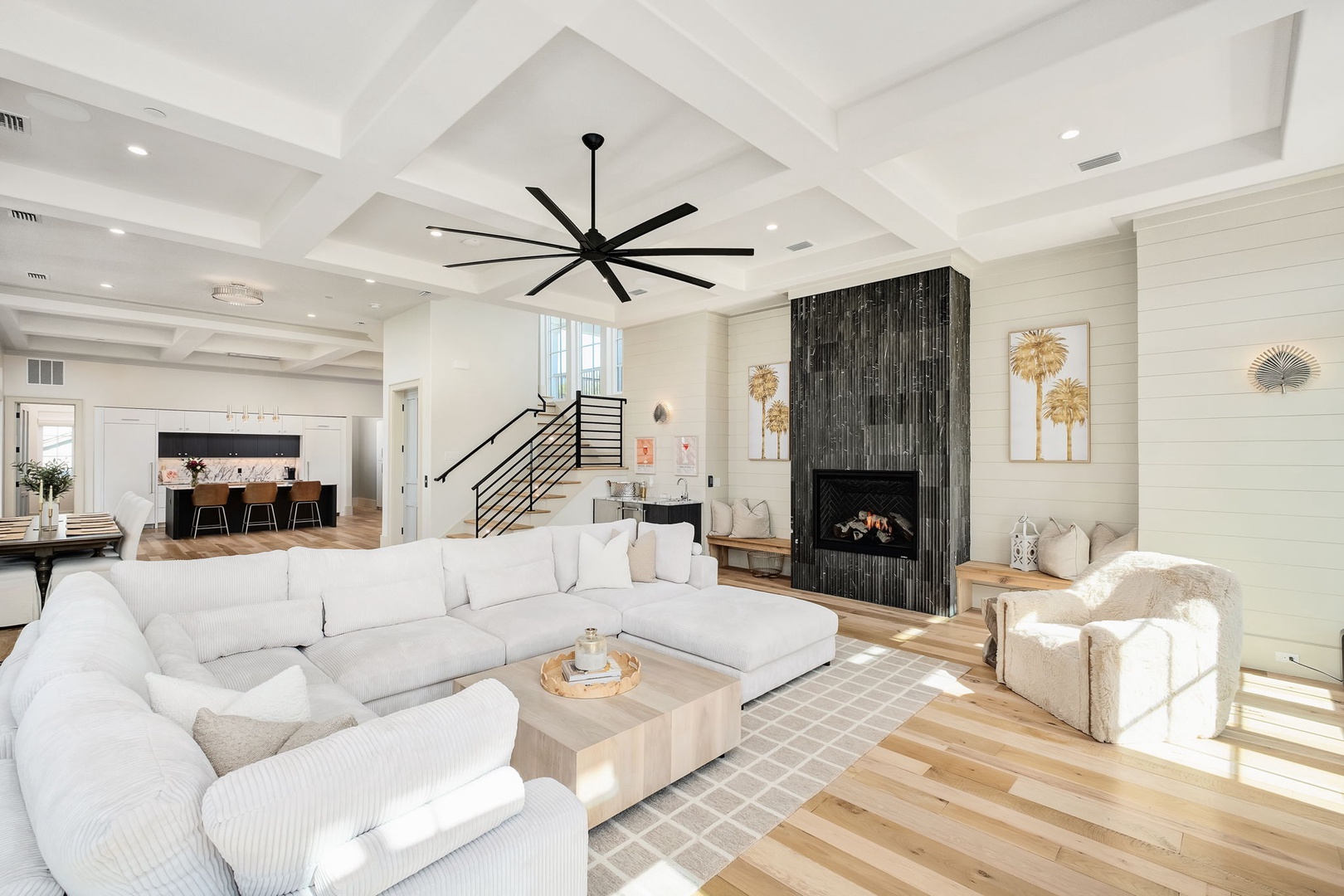 Sink into plush white sectional seating in this bright, airy living space with soaring coffered ceilings and cozy fireplace warmth.