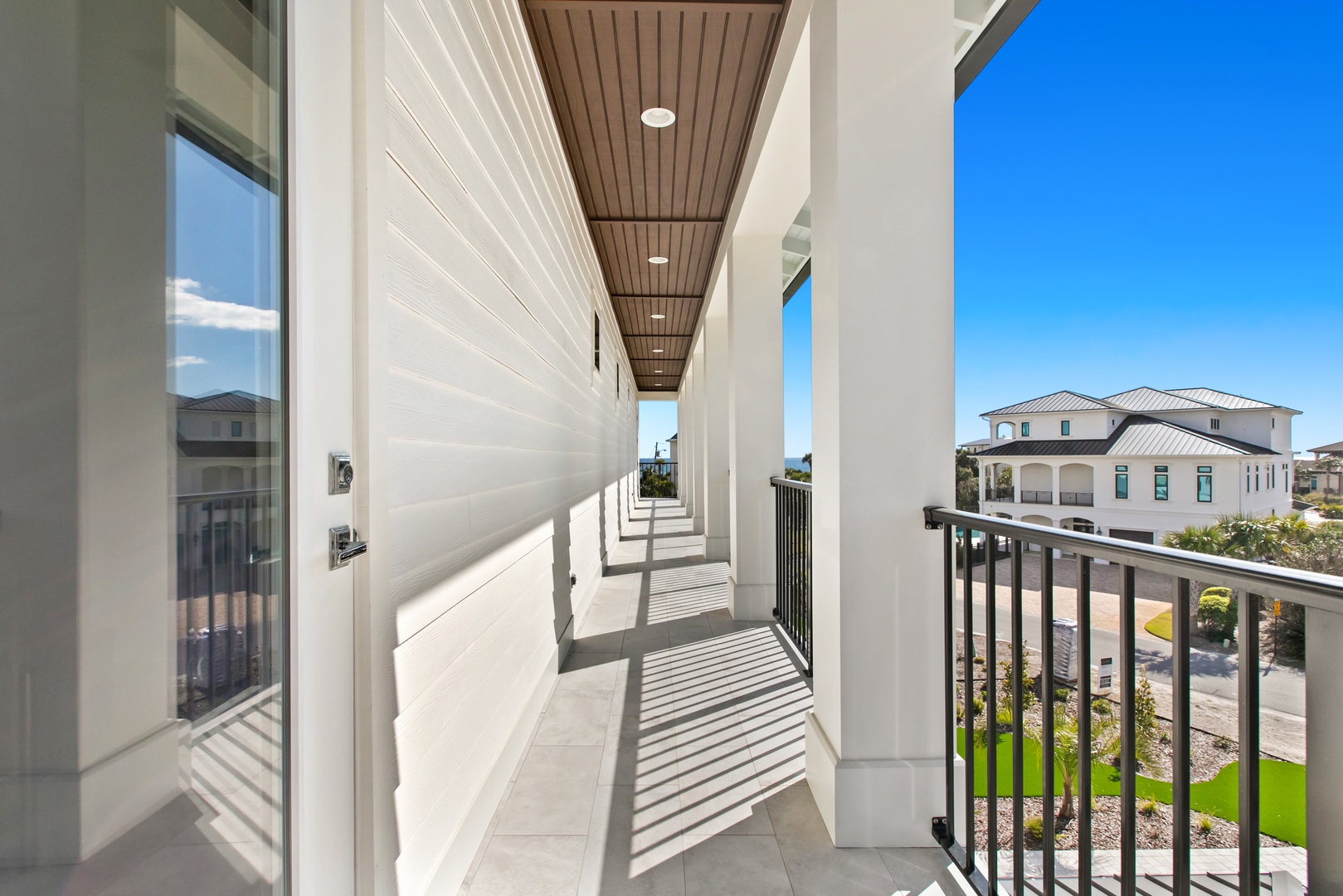 An elevated balcony walkway framed by sleek columns and polished tile, connecting your space to the coastal neighborhood and blue skies beyond.