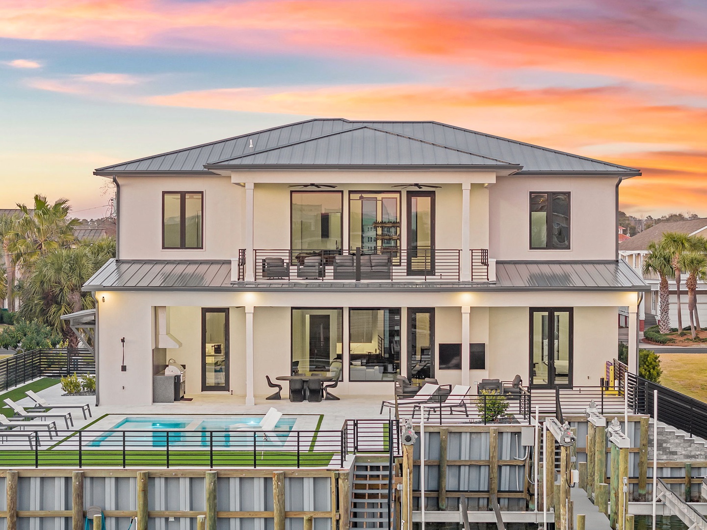 Modern waterfront property with stunning architecture beneath a vibrant sunset sky, showcasing pristine design and coastal elegance.