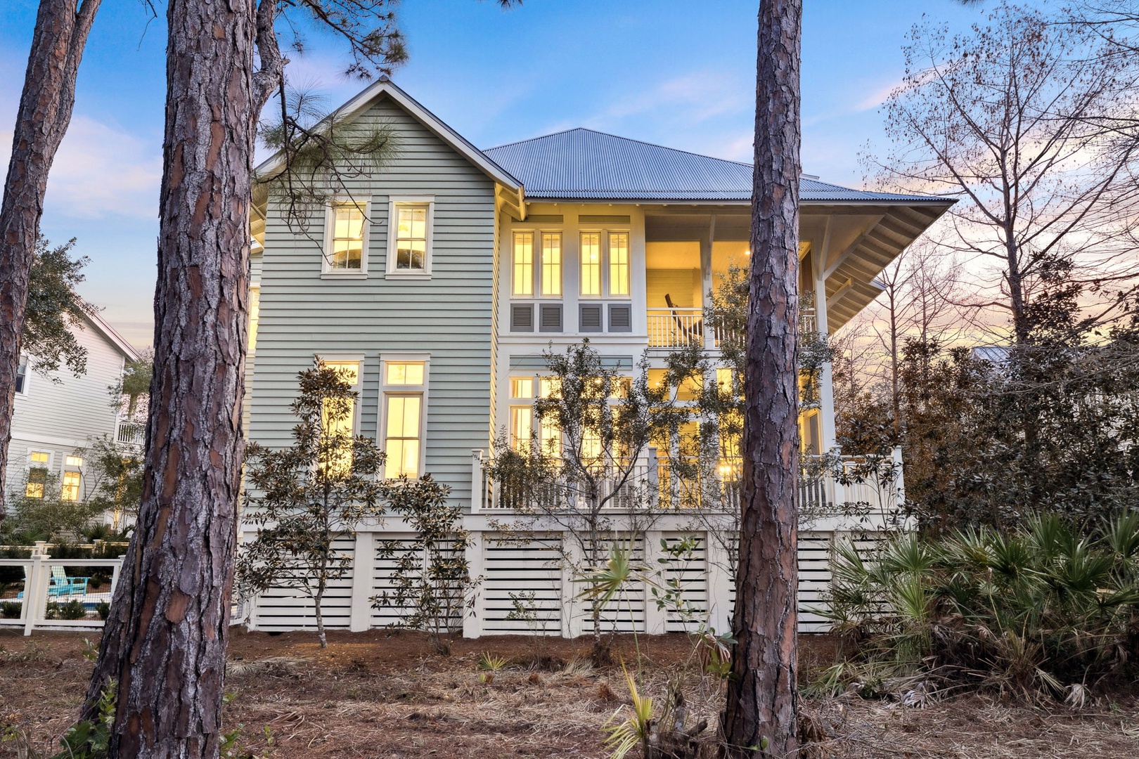 Charming coastal retreat nestled among towering pines, with warm lights welcoming guests to this elegant two-story home featuring wraparound porches.