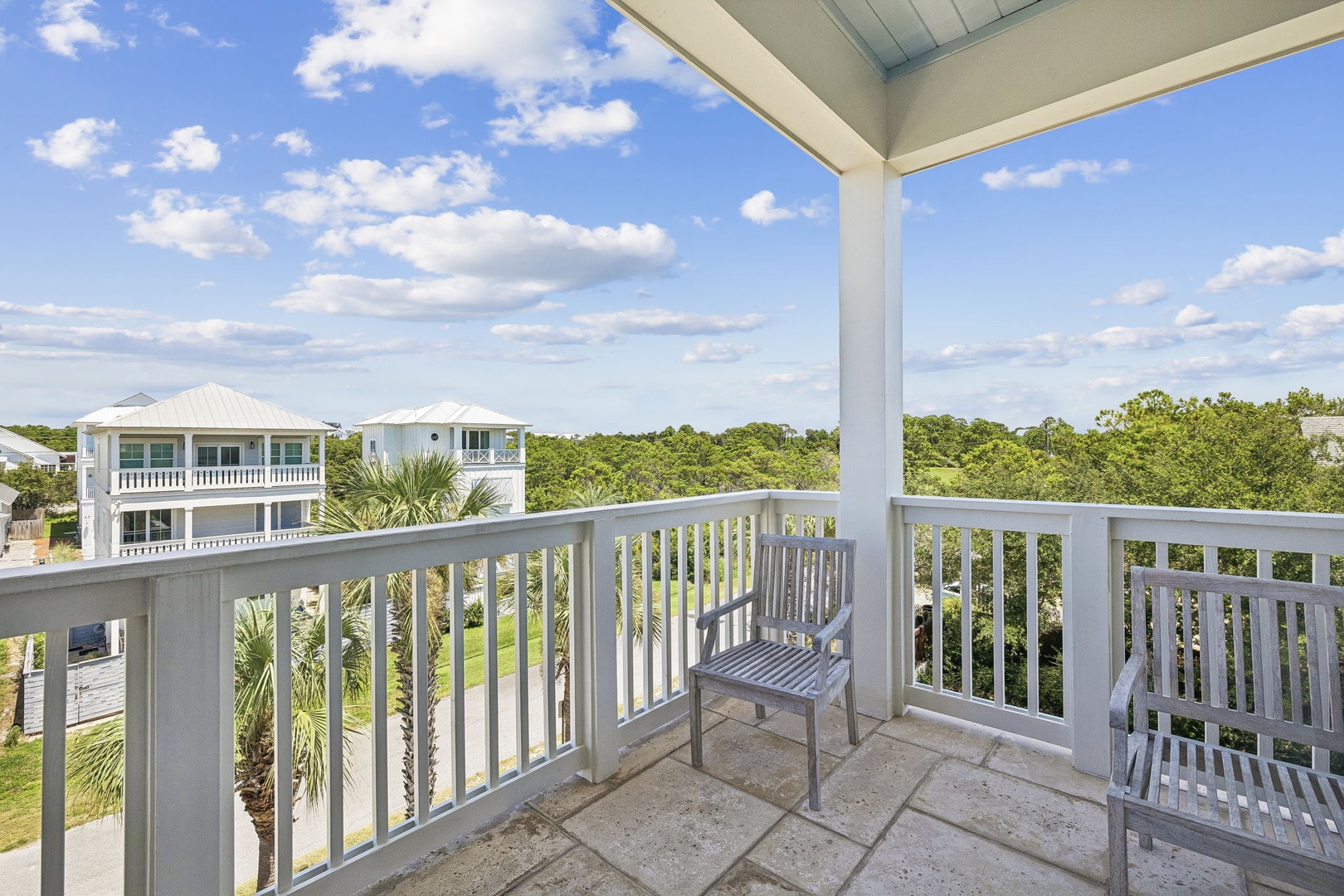 This covered balcony overlooks lush greenery and nearby coastal homes, offering a peaceful spot to soak in the natural beauty of the surrounding area.