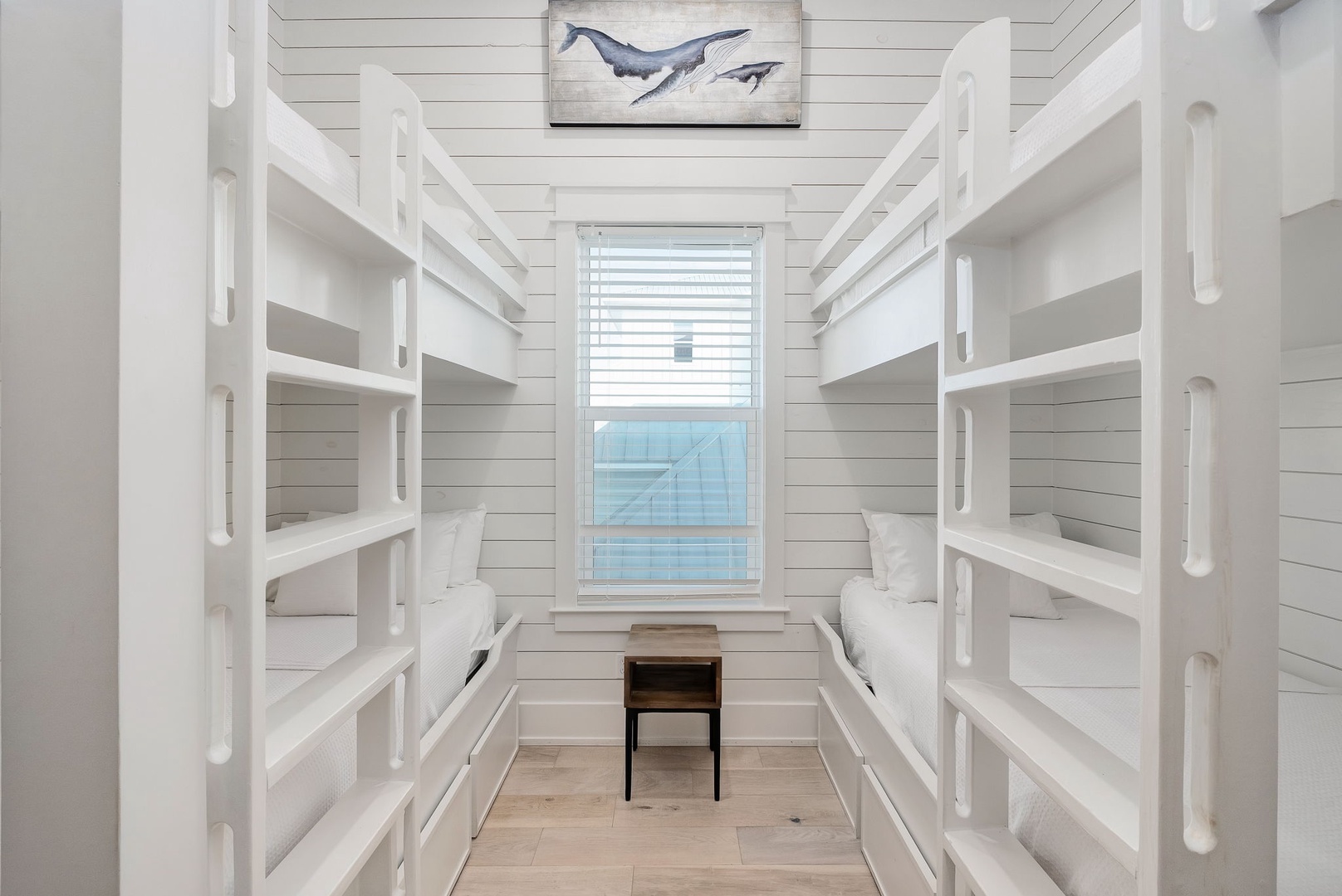 Rest easy in your nautical-themed bunk room where ocean dreams come alive beneath whale artwork and gentle natural light.