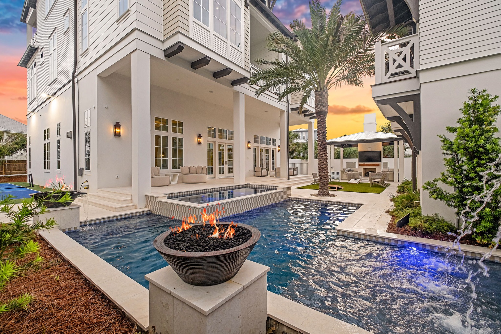 Stunning sunset views illuminate a luxurious backyard oasis, featuring a sparkling pool, hot tub, and fire pit—your perfect retreat for evening relaxation under palm trees and a vibrant sky.