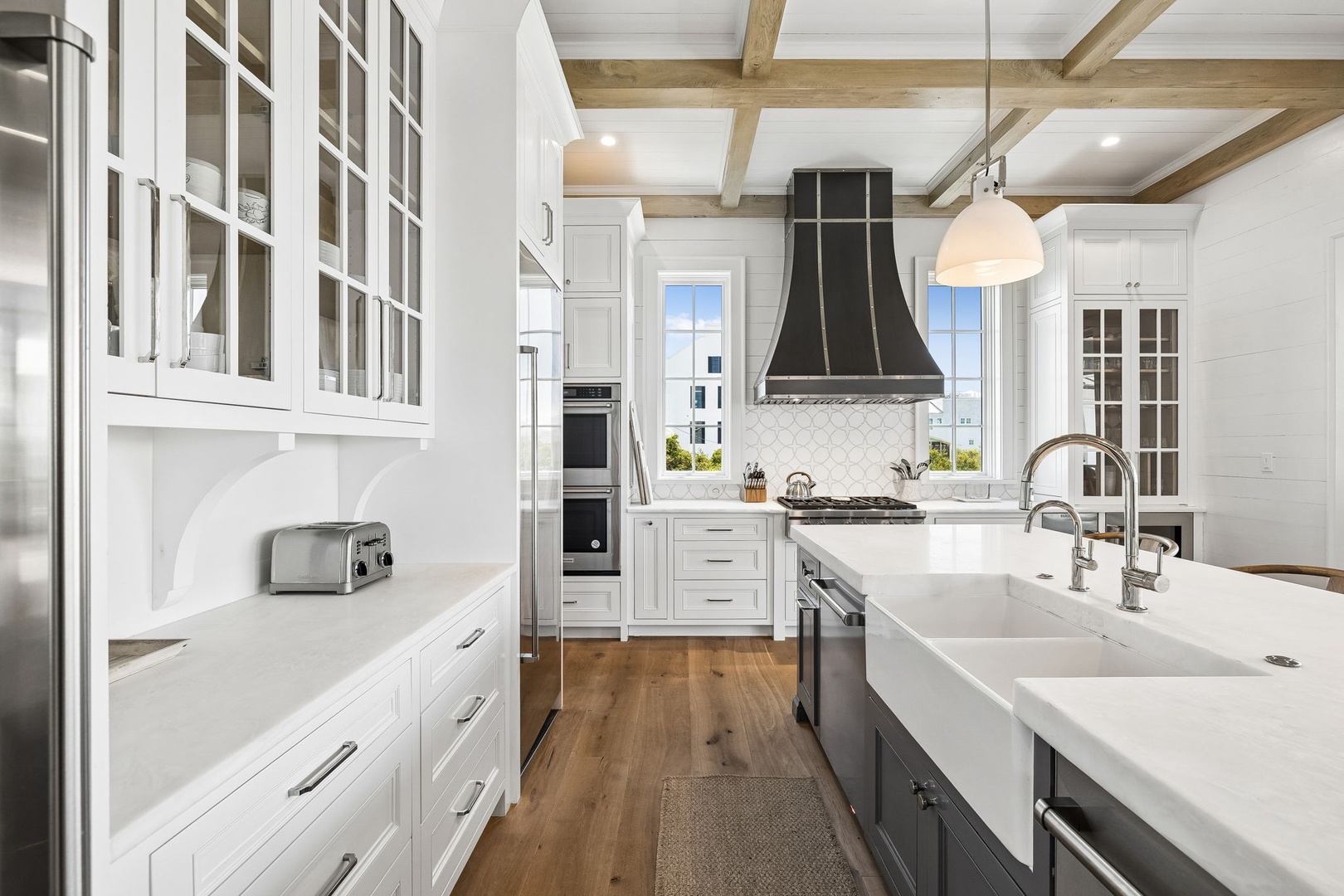 This bright, spacious kitchen features a large island with dual farmhouse sinks, pristine white cabinetry, and rustic exposed beams overhead. You'll love preparing meals here with modern appliances and abundant natural light.