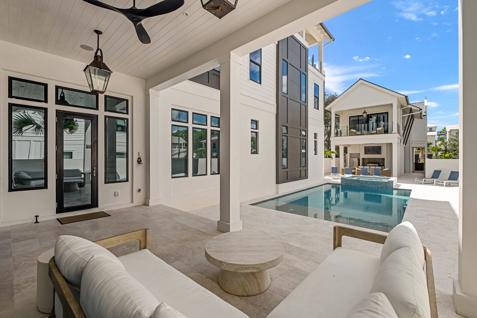 A covered outdoor lounge opens to your private pool and modern courtyard, framed by bright Florida skies. Relax on cushioned seating under the ceiling fan, perfect for sunny days and balmy evenings.